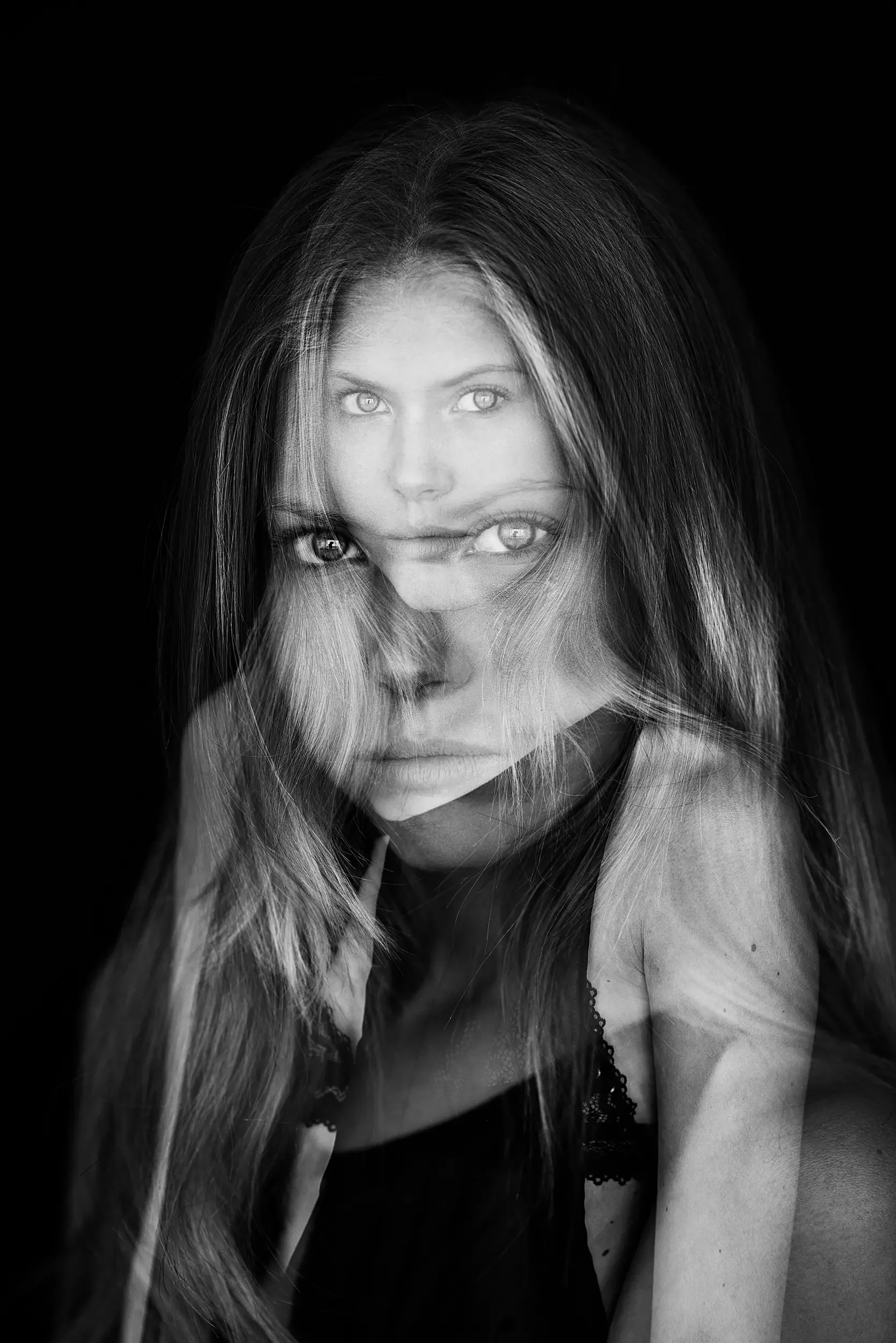 Black and white photo of a woman with long hair, featuring a double exposure effect of her face and her reflection.