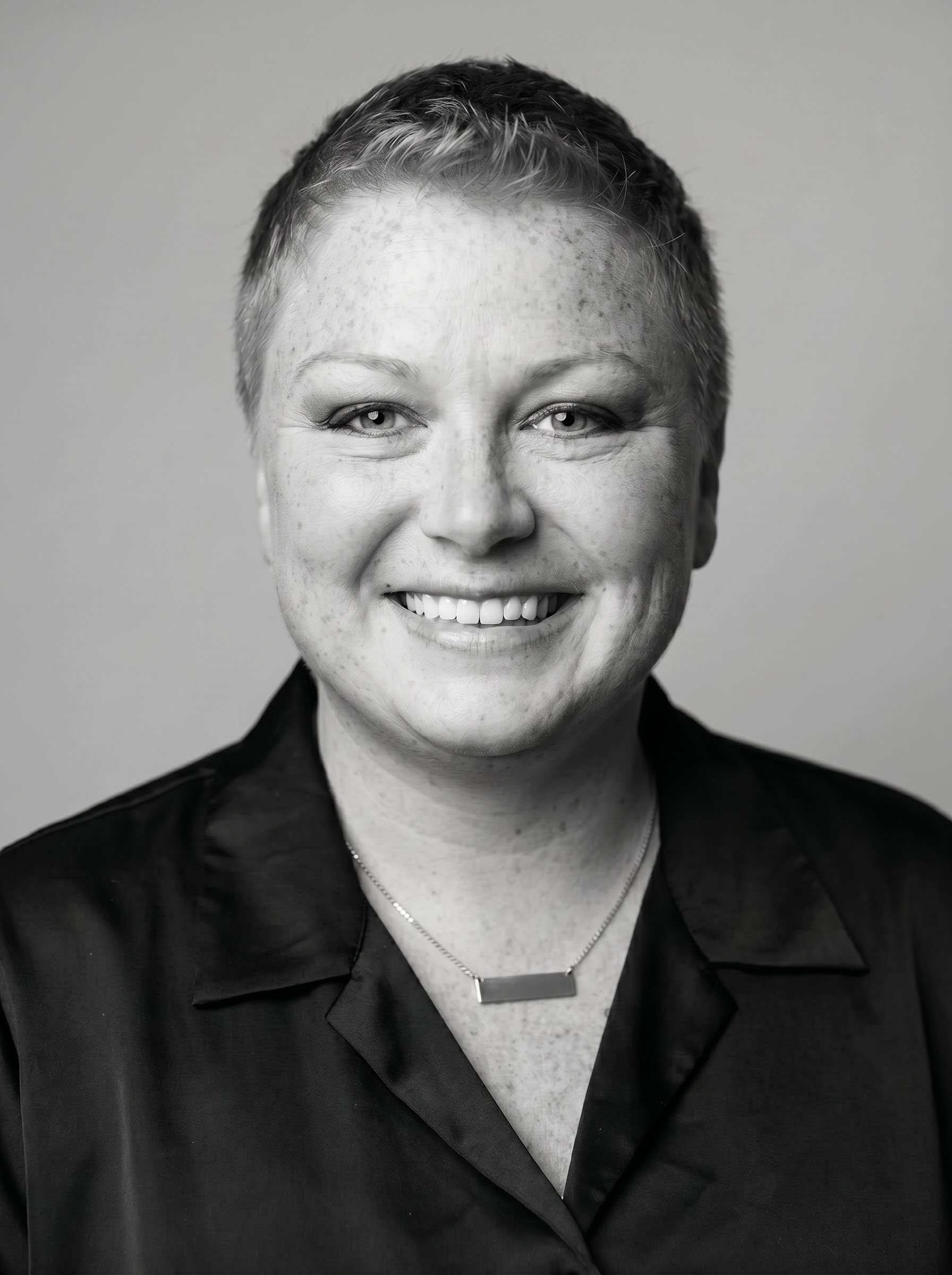Black and white portrait of the author Blake Morgan a smiling woman with short, hair wearing a dark jacket, a necklace, and a rectangular pendant.