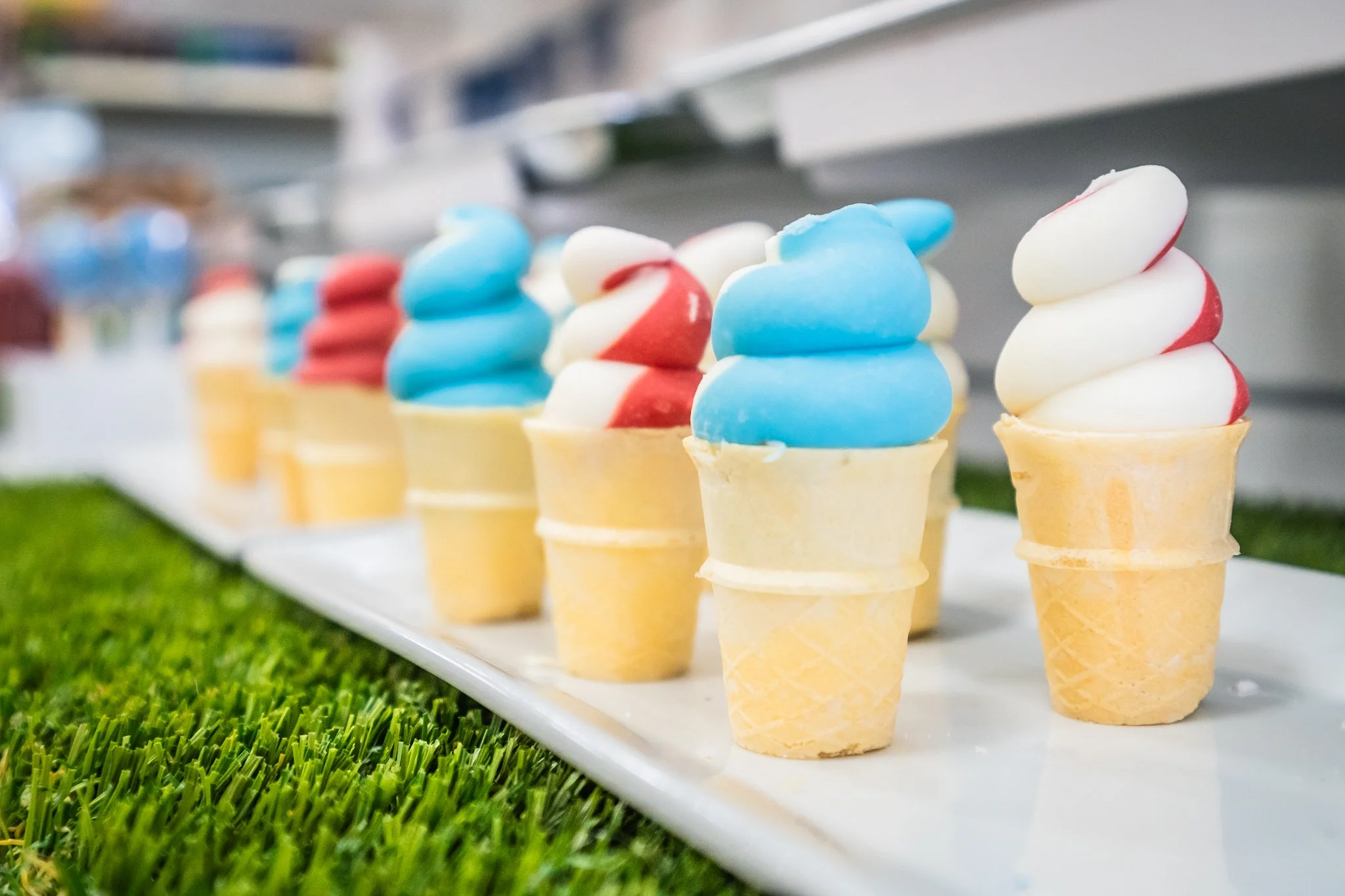 Multiple colorful ice cream cones displayed on a white tray at an outdoor event with grass in the foreground.