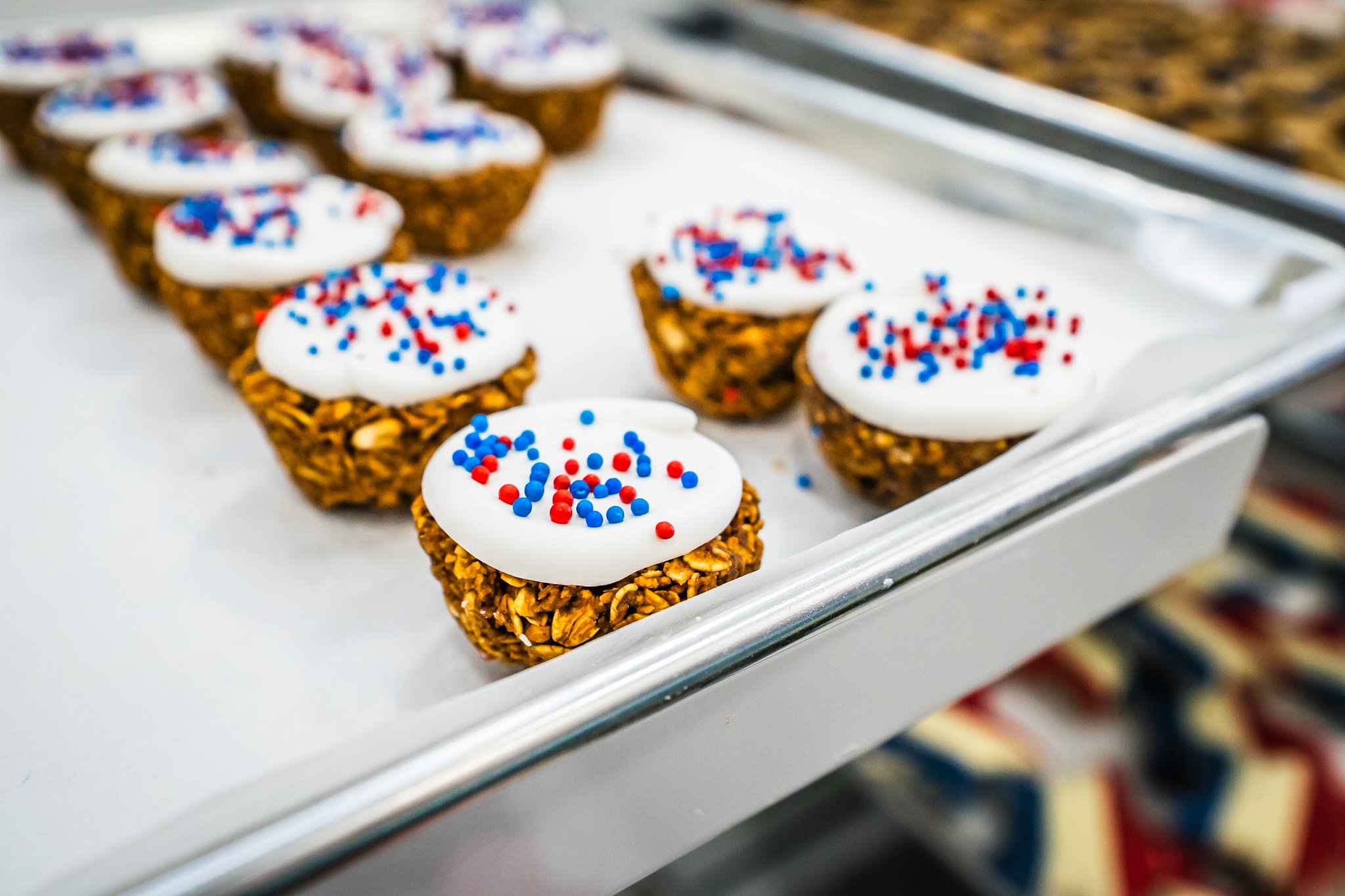 Close-up of small dessert cups topped with white icing and red, white, and blue sprinkles, arranged on a white tray.