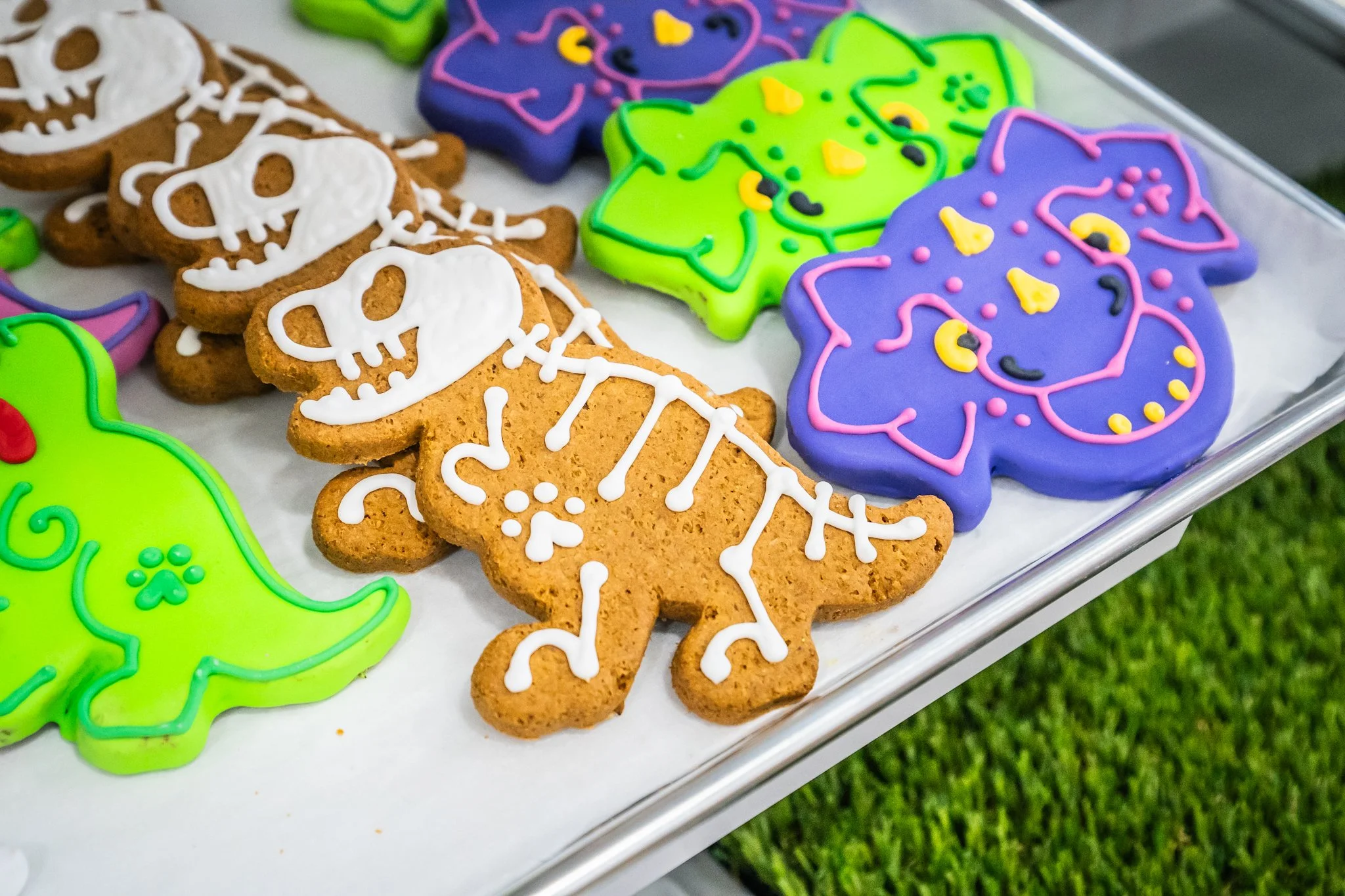 Colorful Halloween-themed decorated cookies on a tray, including gingerbread skeletons with white icing, and lights with purple, green, and purple icing designs.