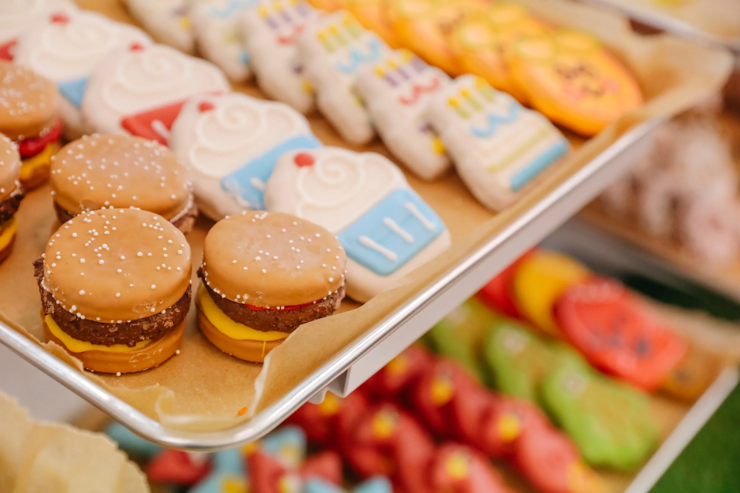 Close-up of decorative cookies shaped like hamburgers and soda cups on display at a bakery or store.