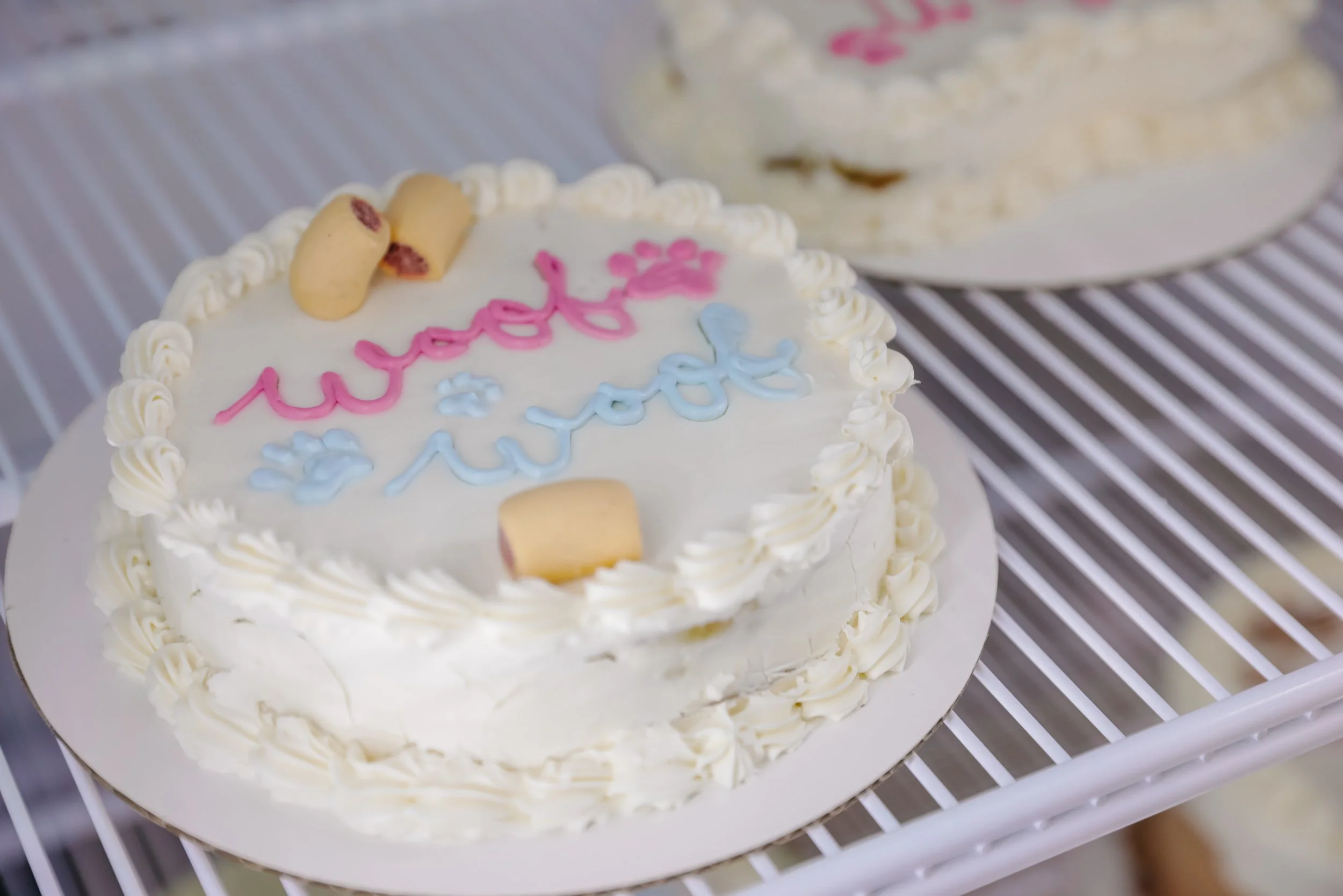 White birthday cake decorated with pink and blue icing, featuring the message "happy birthday" written on top, topped with small yellow cookies.