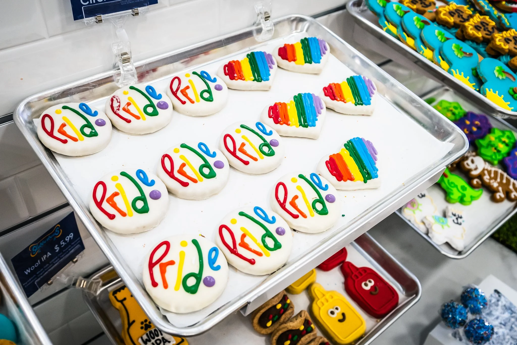 Cookies decorated with white icing spelling 'Feliz' and rainbow stripes, arranged on a tray in a store display.