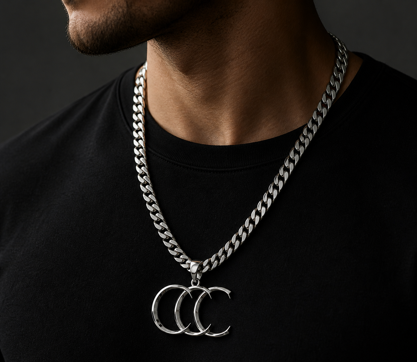 A man wearing a black shirt and a silver chain necklace with a triple moon pendant.