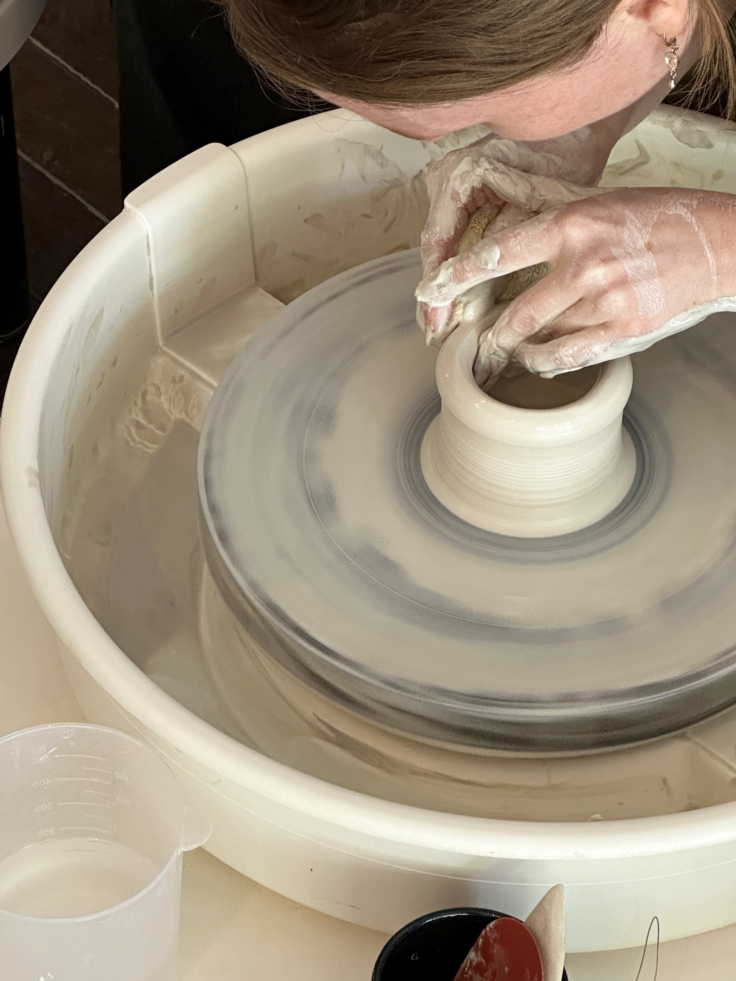 Person shaping clay on a pottery wheel in a ceramics studio.
