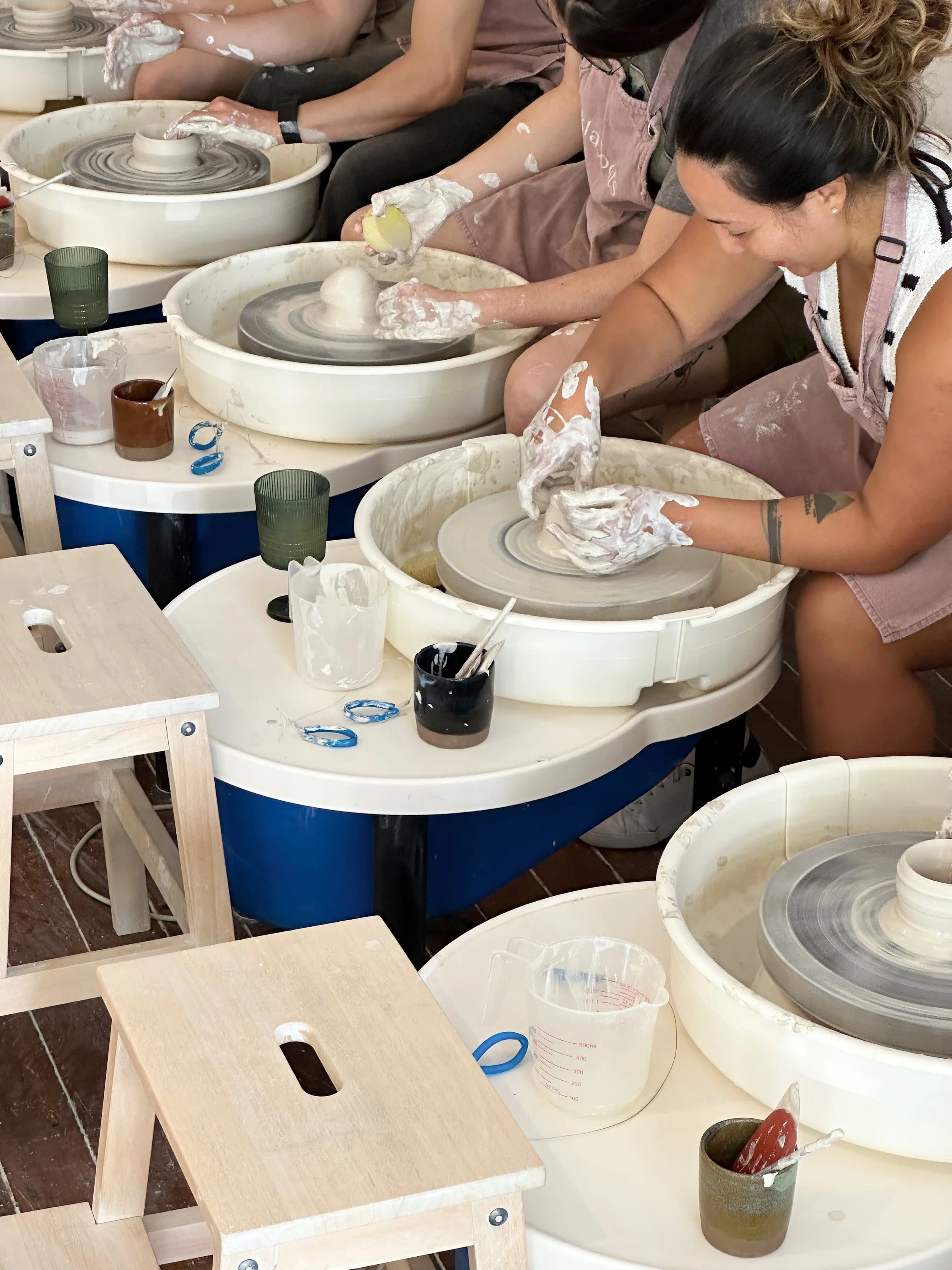 People sitting at pottery wheels shaping clay into vessels in a pottery class