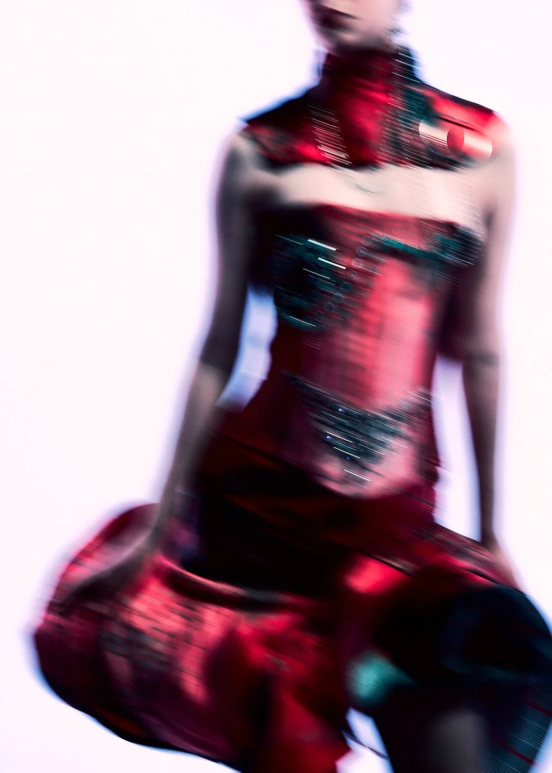 Blurred image of a woman wearing a red and black dress, sitting and leaning forward.