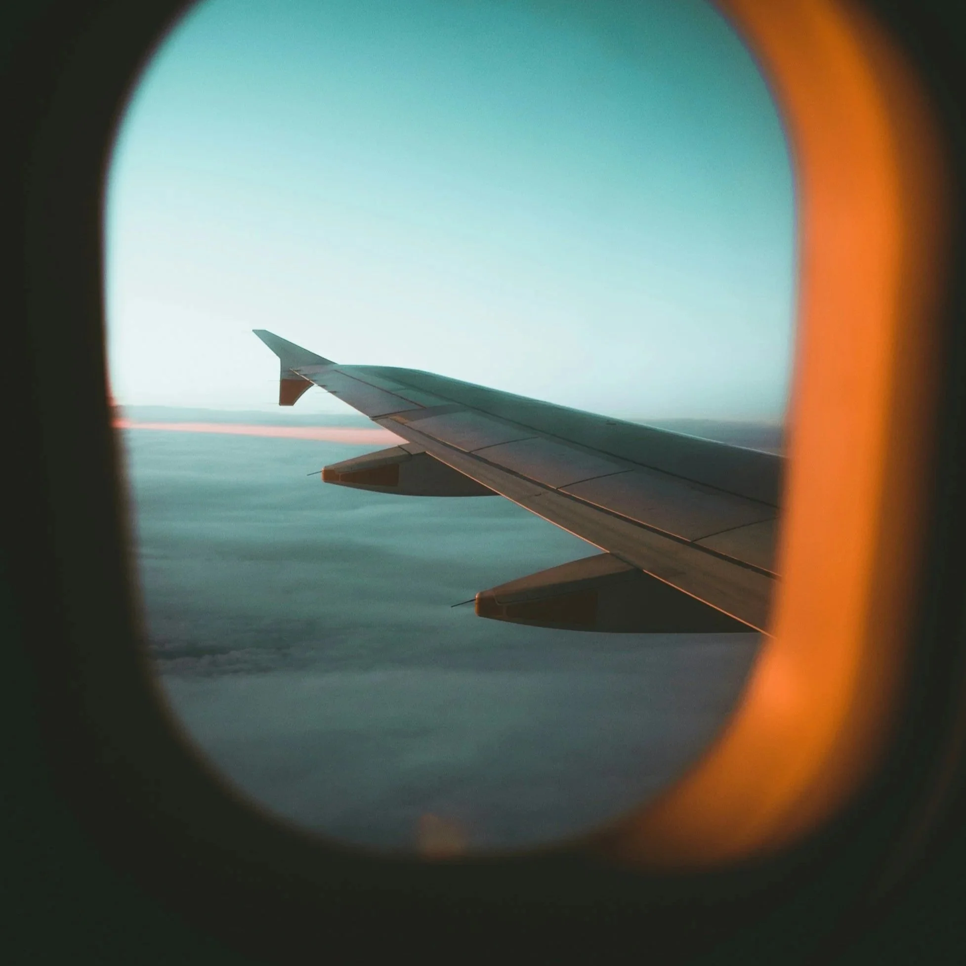 A plane wing from the window of an airplane overlooking an ocean