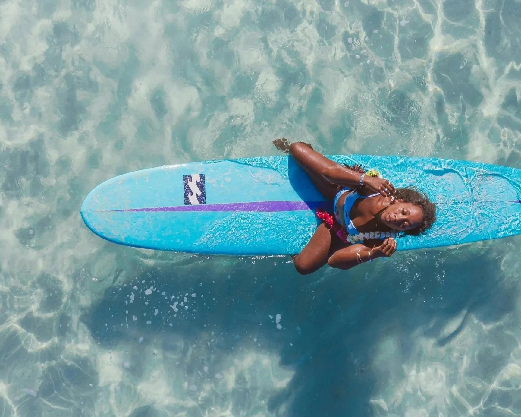 Woman resting on a surfboard in clear water.
