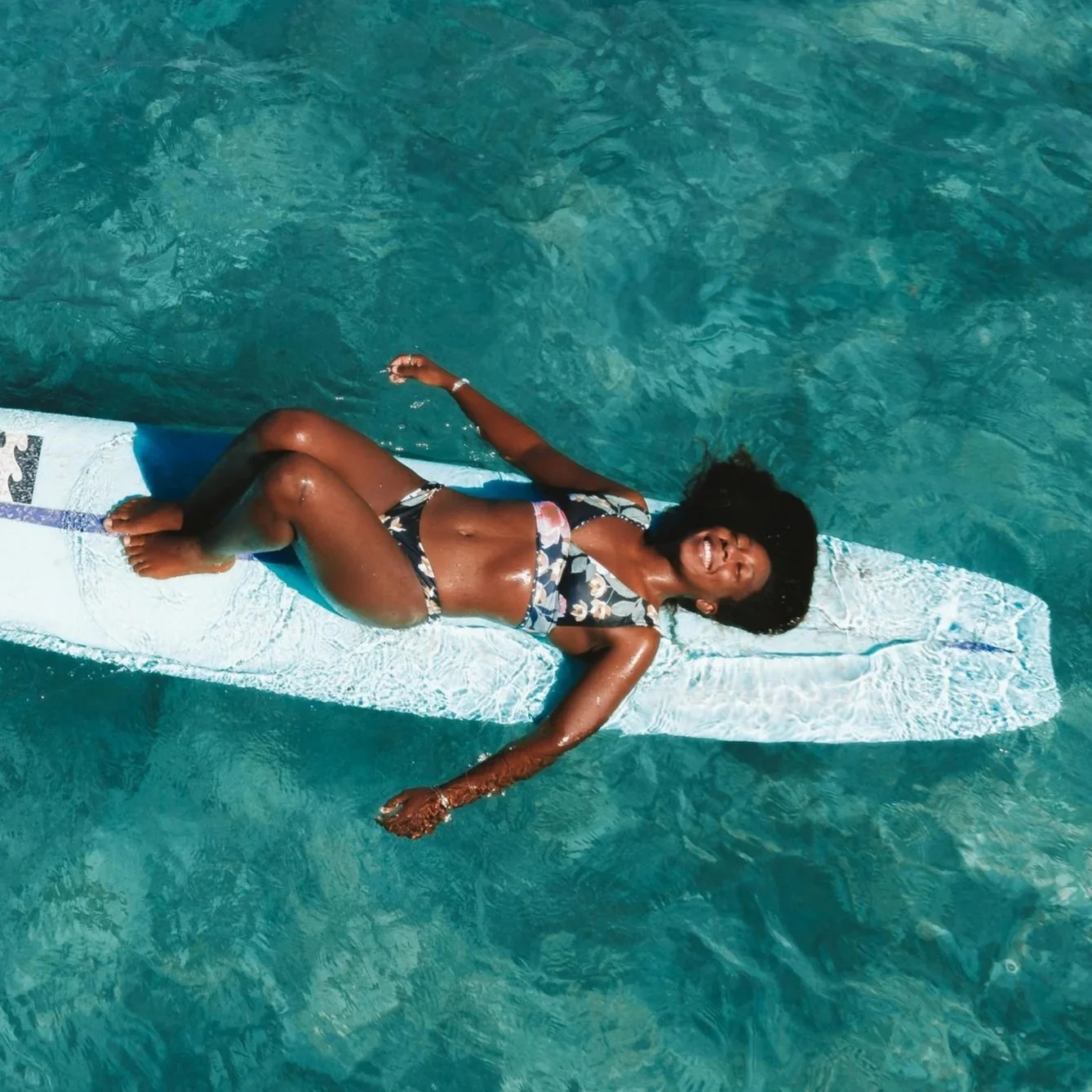 Woman floating on a surfboard in clear blue water.