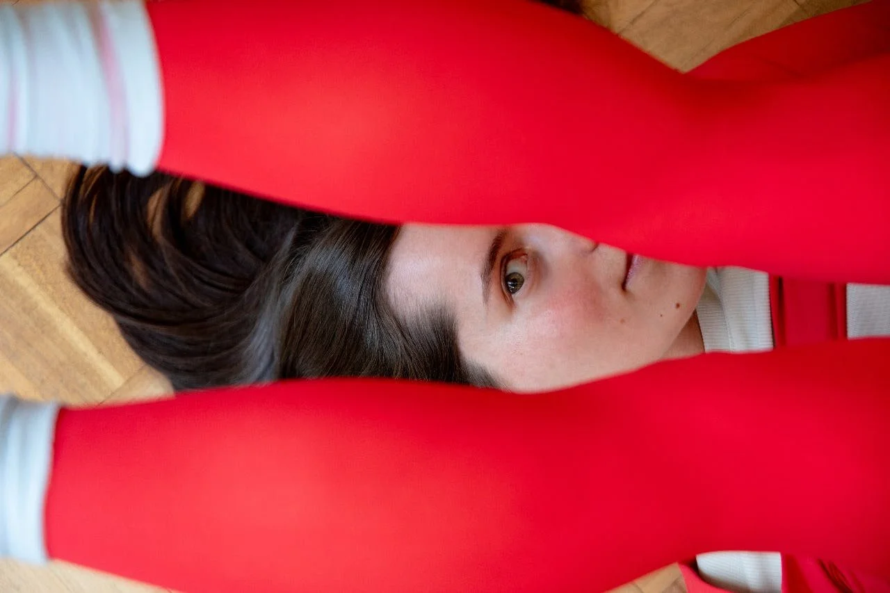 Woman lying on floor in red tights during embodied movement practice.