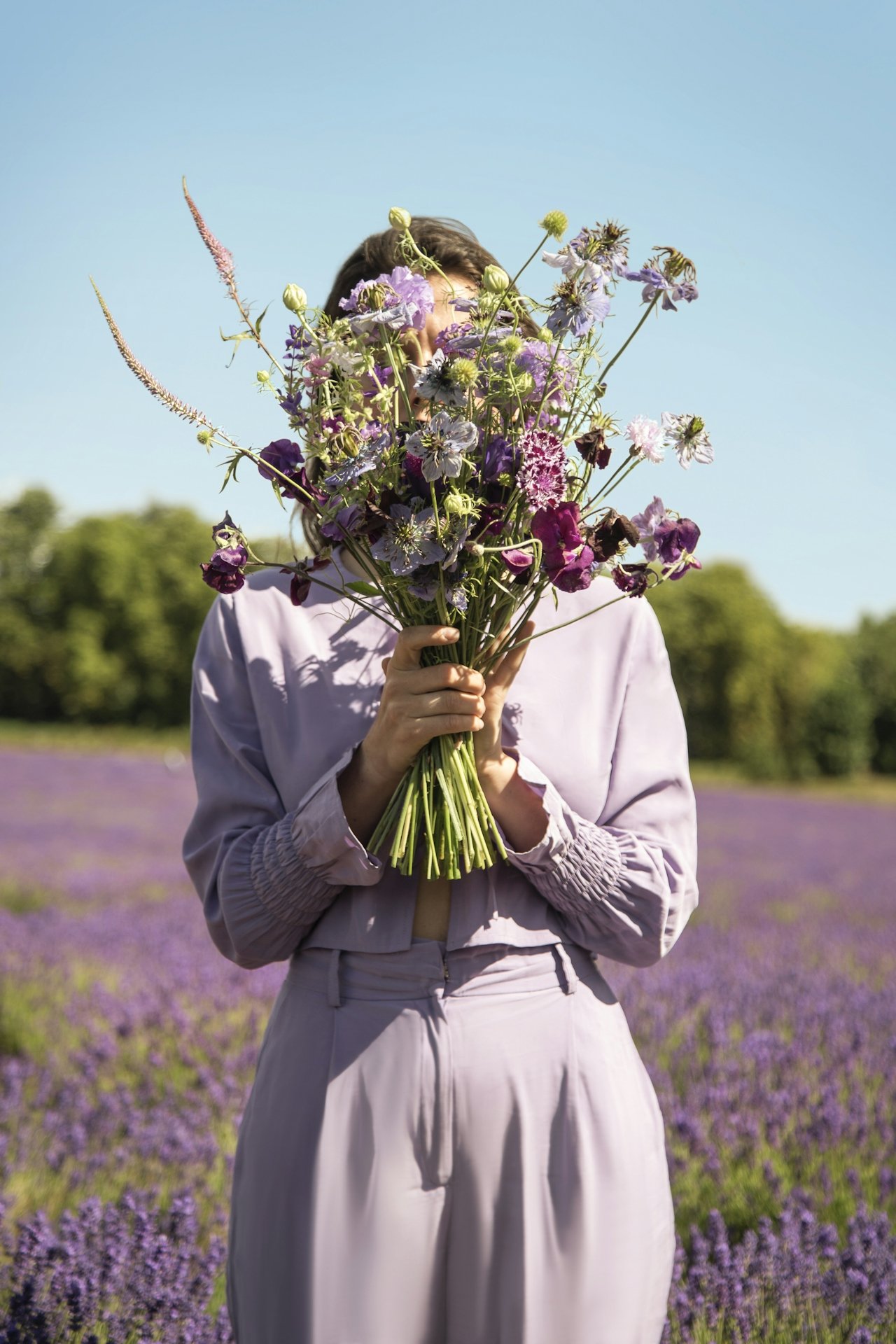 Woman holding wildflowers in a lavender field beneath open sky.