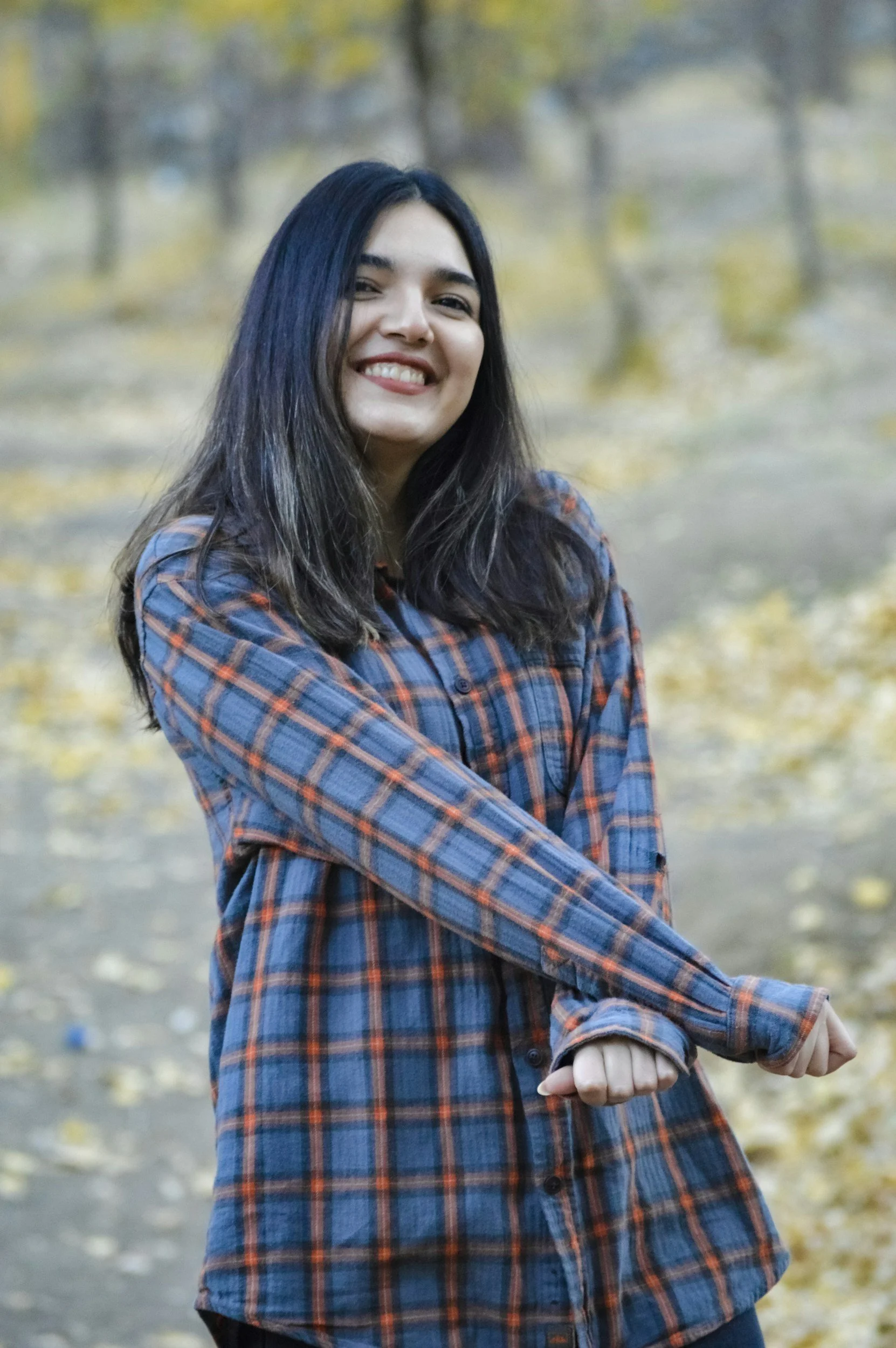 Girl in her late teens, with long black hair wearing a flannel. Happily, confidently smiling into the camera.