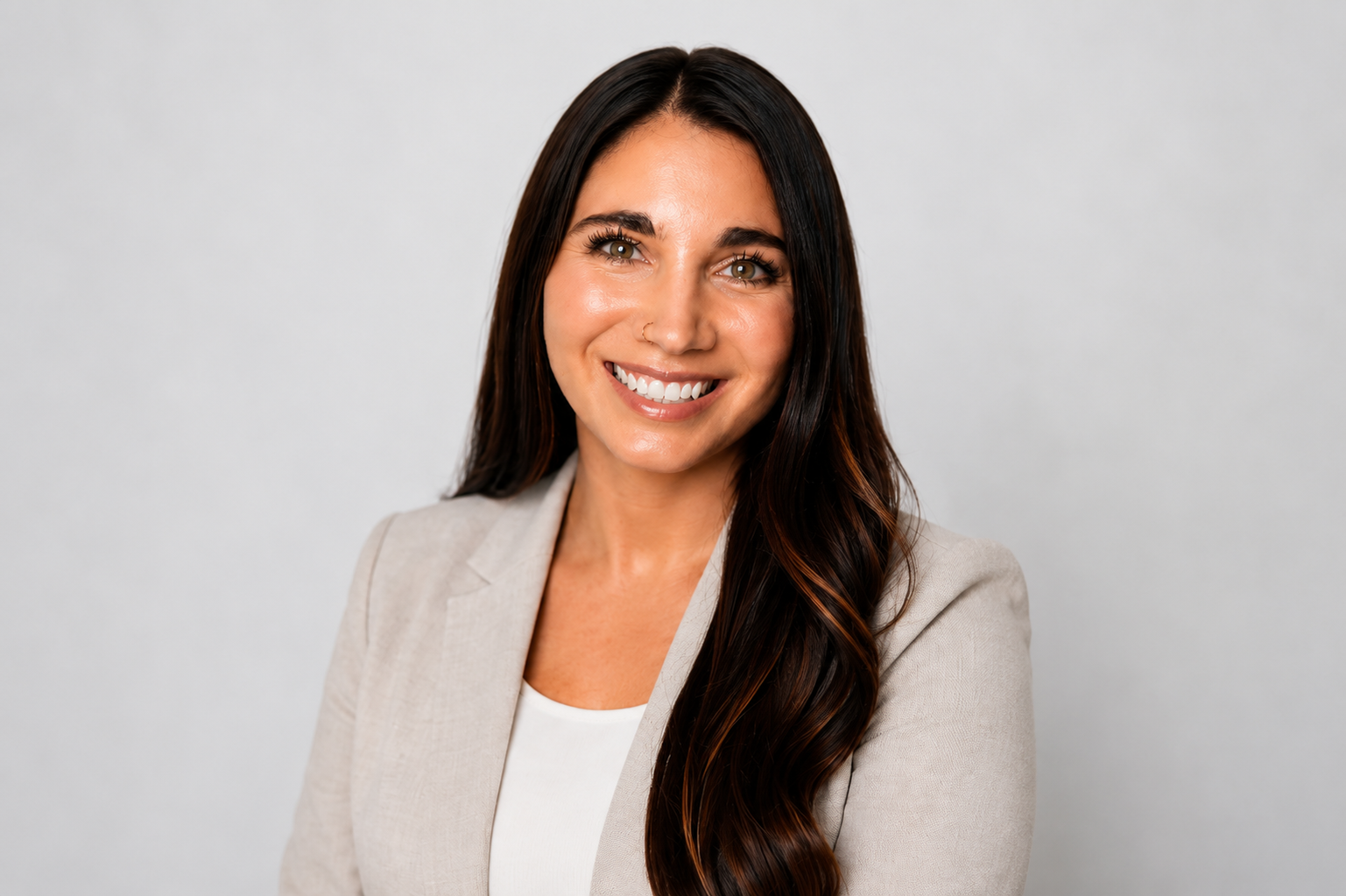 A portrait of a smiling woman with long dark hair, wearing a beige blazer and white top, against a plain light background.
