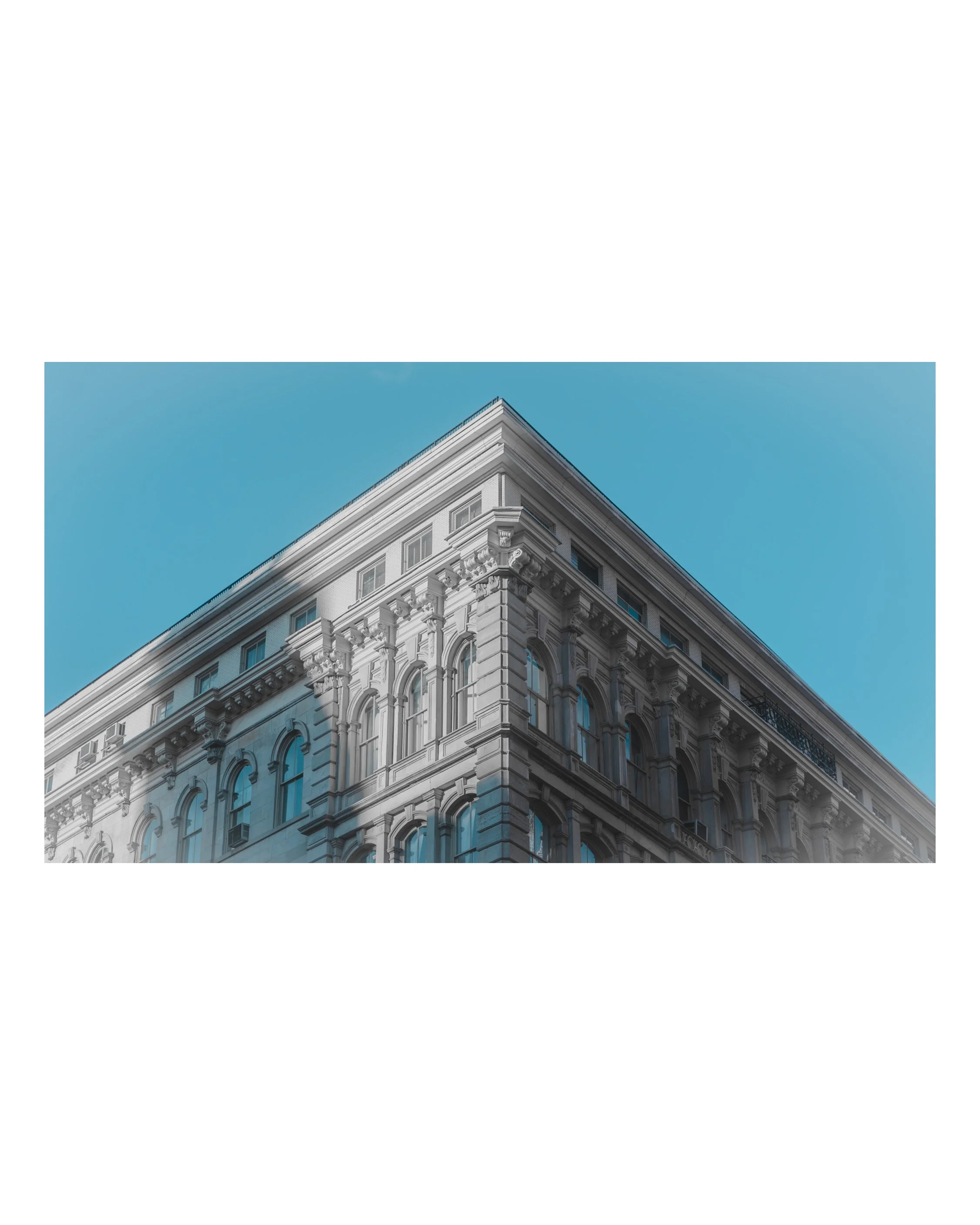 The corner of a tall historic building with ornate architectural details, set against a clear blue sky.