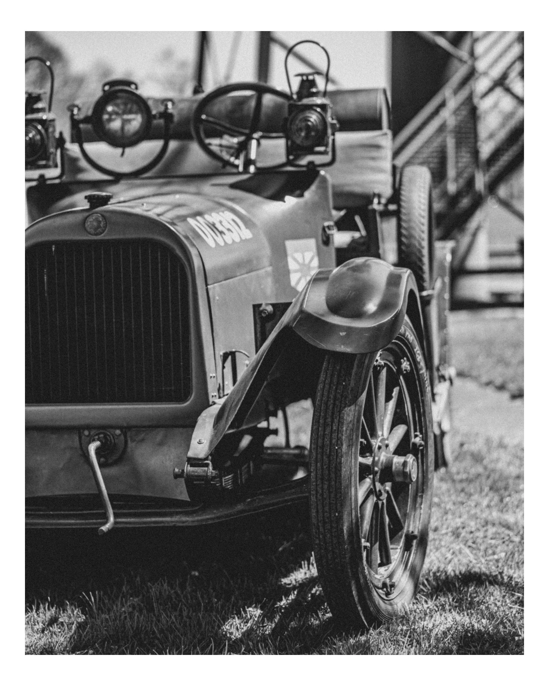 A black and white photograph of a vintage car with a boat loaded on its trailer, parked on a grassy field.