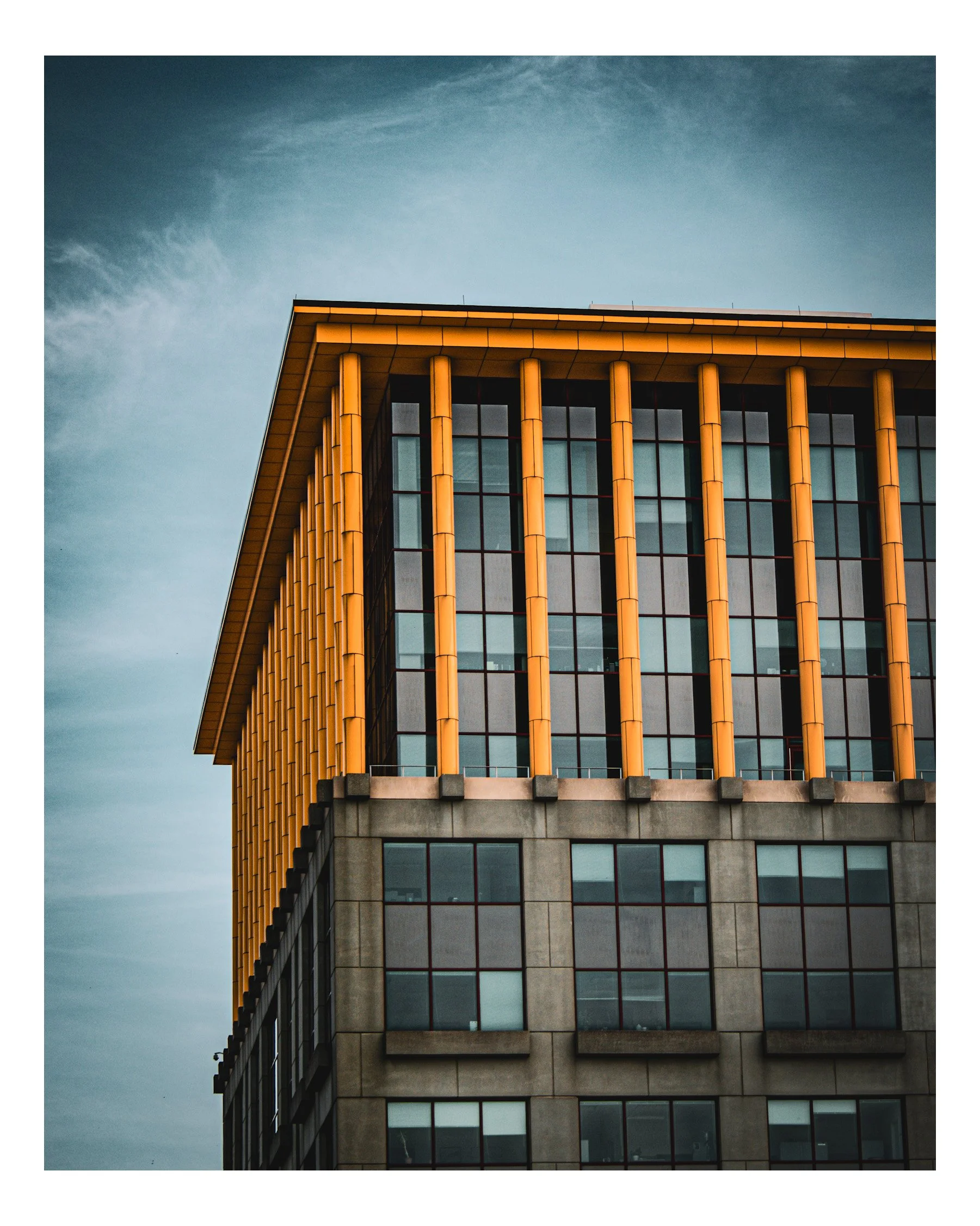 Close-up view of a modern office building with yellow vertical architectural elements and glass windows, set against a cloudy sky.