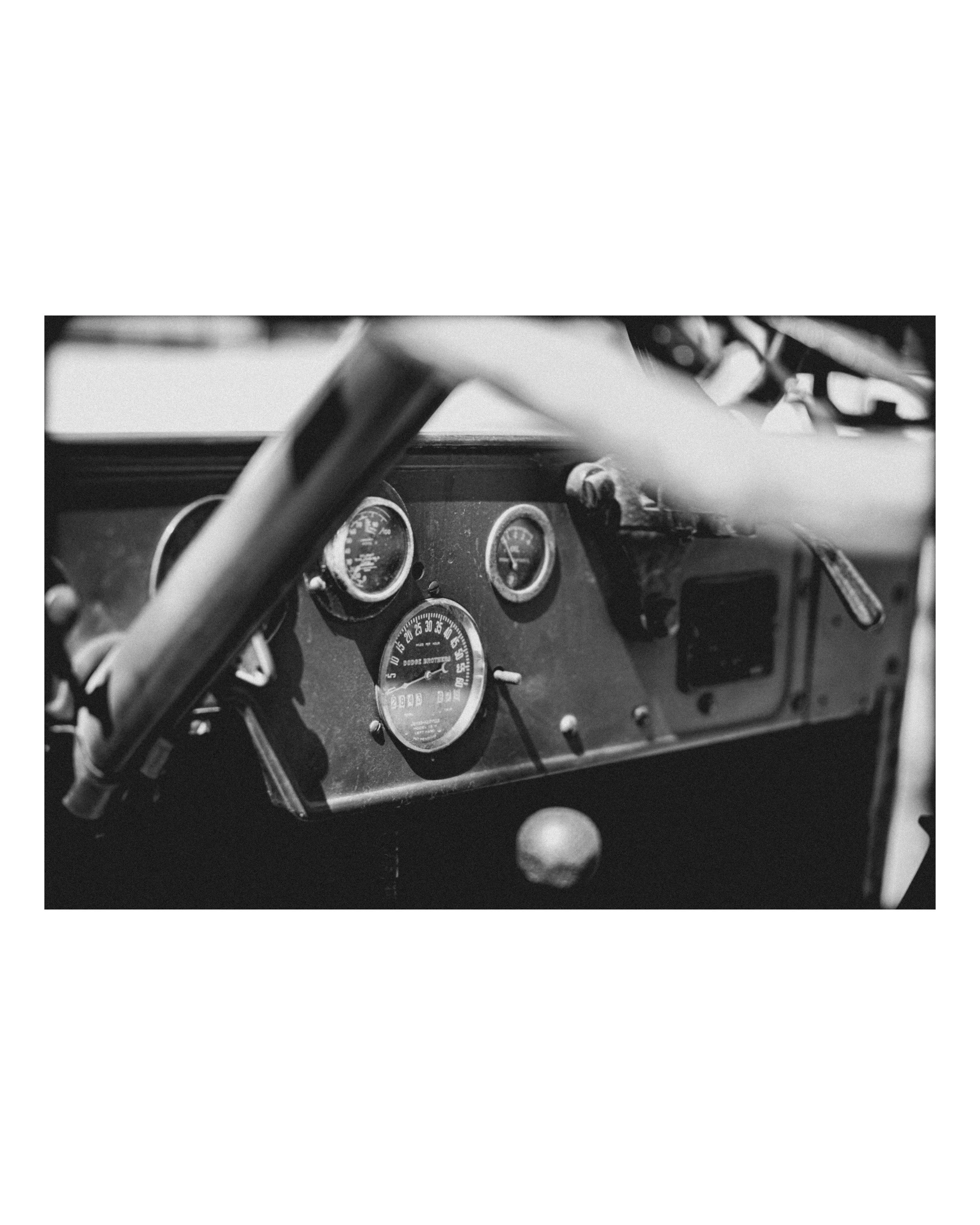 Black and white photo of a vintage car dashboard, showing detailed speedometer, gauges, and part of the steering wheel.
