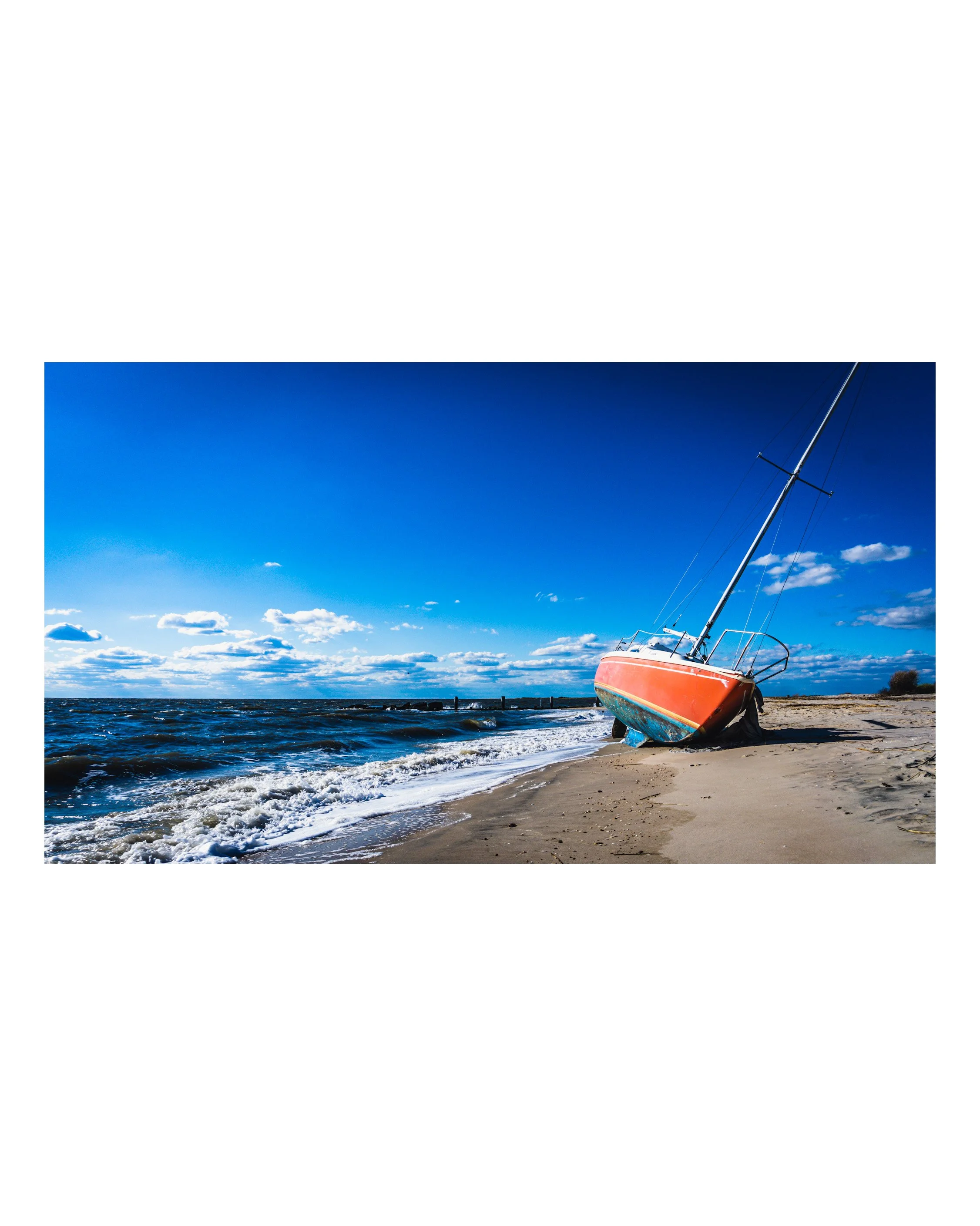 A sailboat beached on sandy shore with blue sky and scattered clouds, water waves in foreground.