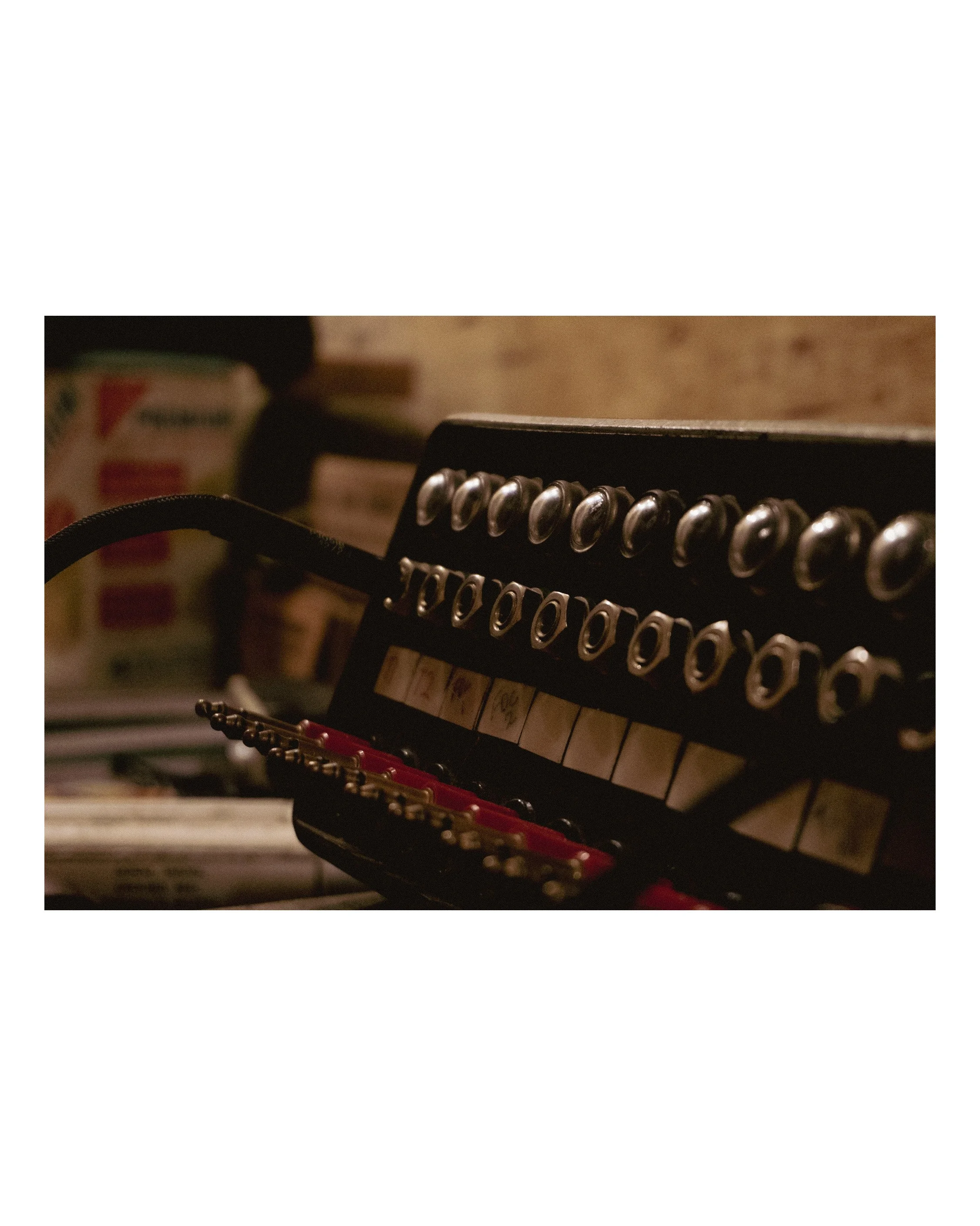 Close-up of a piano with a row of metal tuning pegs and part of a musical note decal, with a background showing a blurry vintage-style wall.