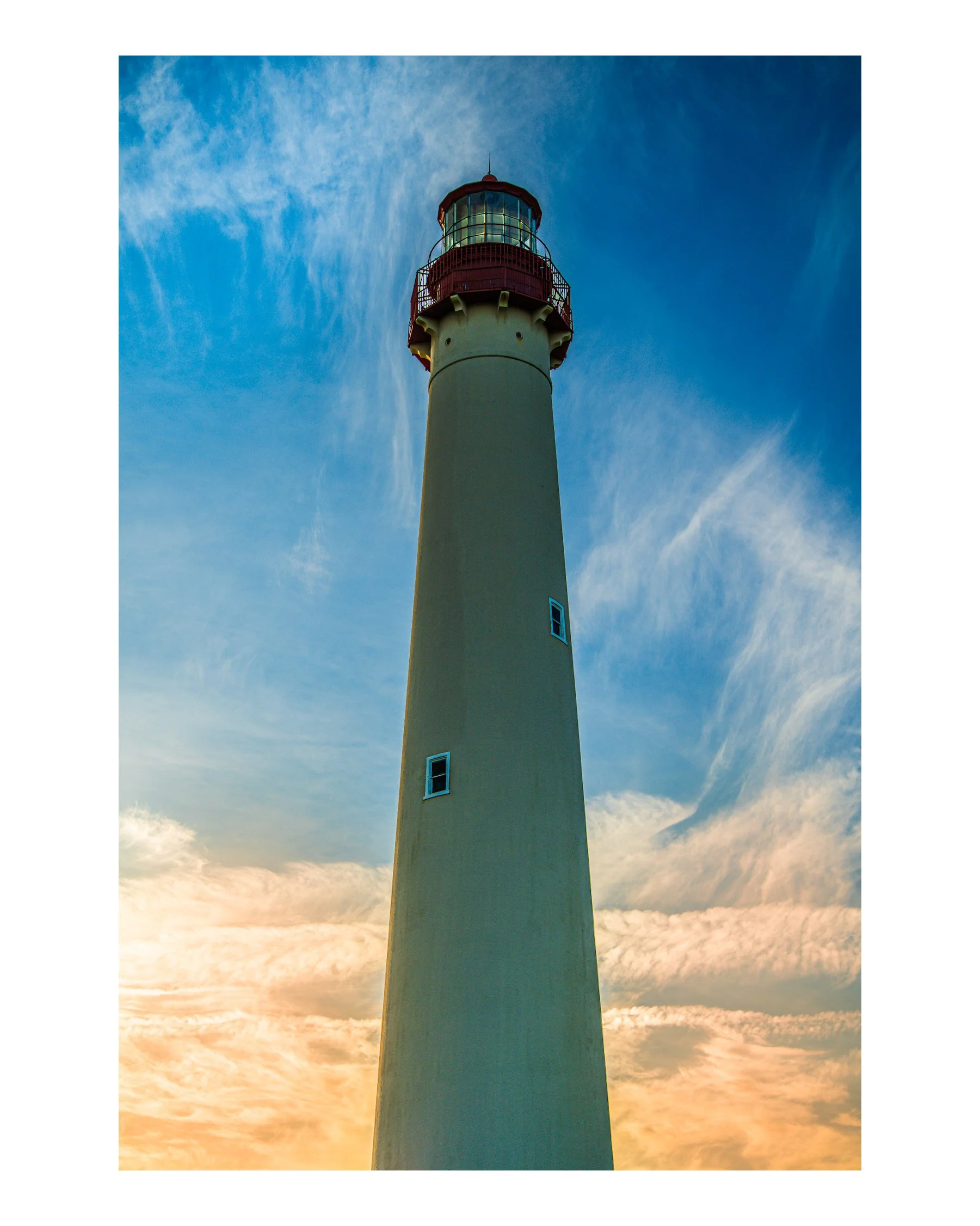 A lighthouse during sunset, standing tall against a partly cloudy sky with shades of orange, pink, and blue.