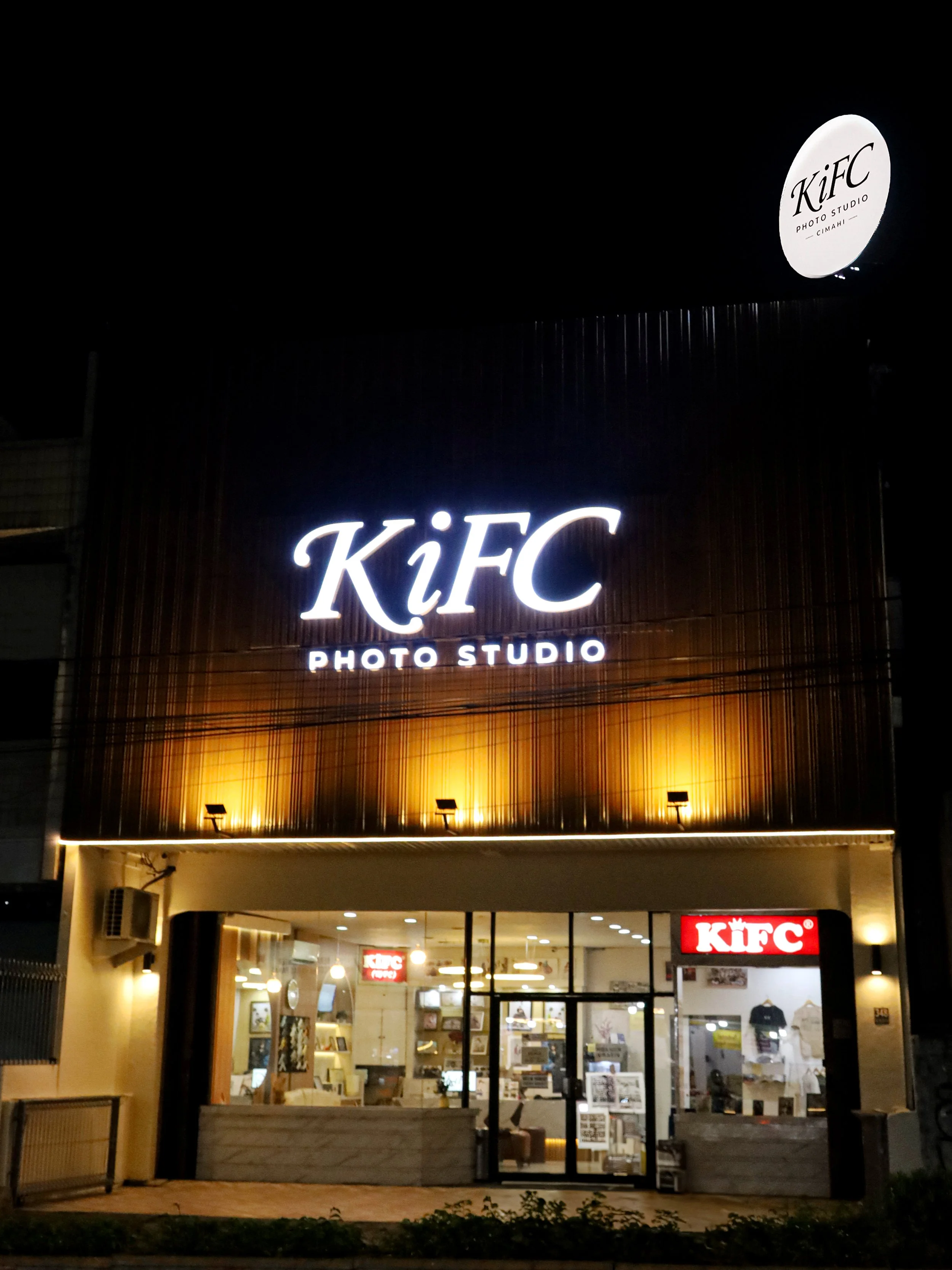 Nighttime view of a KFC restaurant with illuminated signs and interior visible through large glass windows.