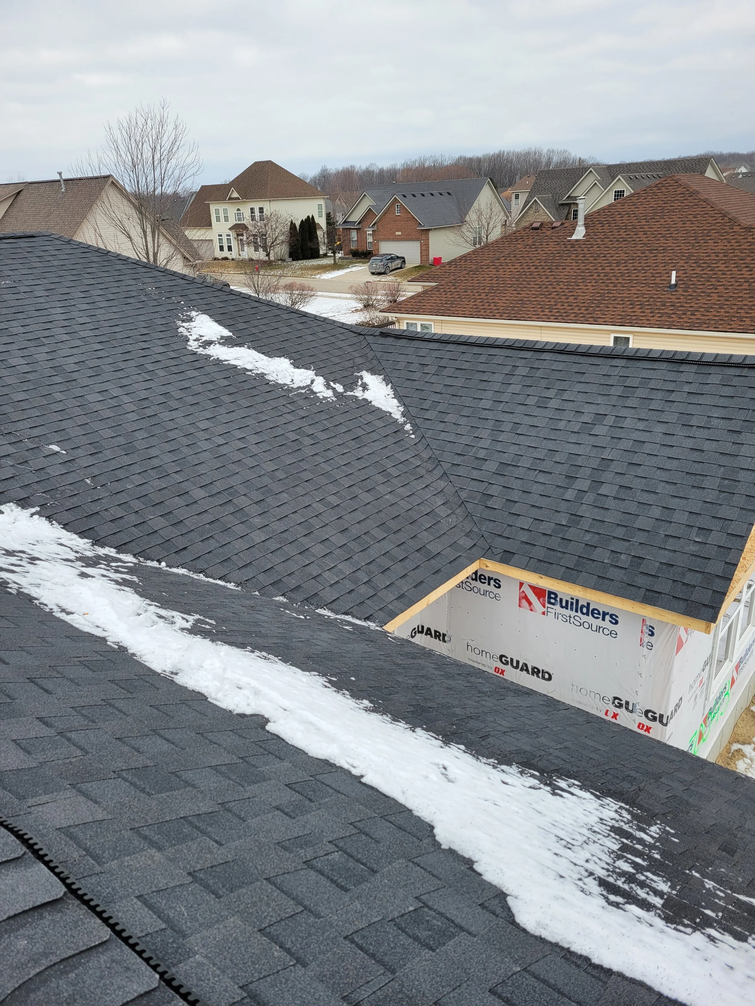 View from a rooftop showing neighboring houses in a suburban neighborhood with snow on the roofs and ground.