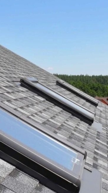 Three solar panels installed on a sloped roof with gray shingles, with trees and a blue sky in the background.