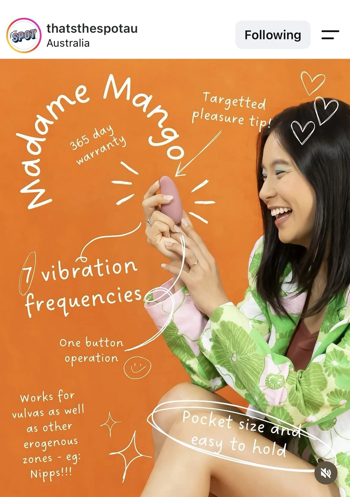A woman with dark hair smiling and holding a small pink device. The background is orange with white handwritten notes about the device's features, including 'Madame Mango,' '365 day warranty,' 'targeted pleasure tip,' 'vibration frequencies,' and 'one button operation.' The notes also mention its effectiveness for vulvas and other erogenous zones, and that it is pocket-sized and easy to hold. The woman is wearing a green and pink floral shirt.