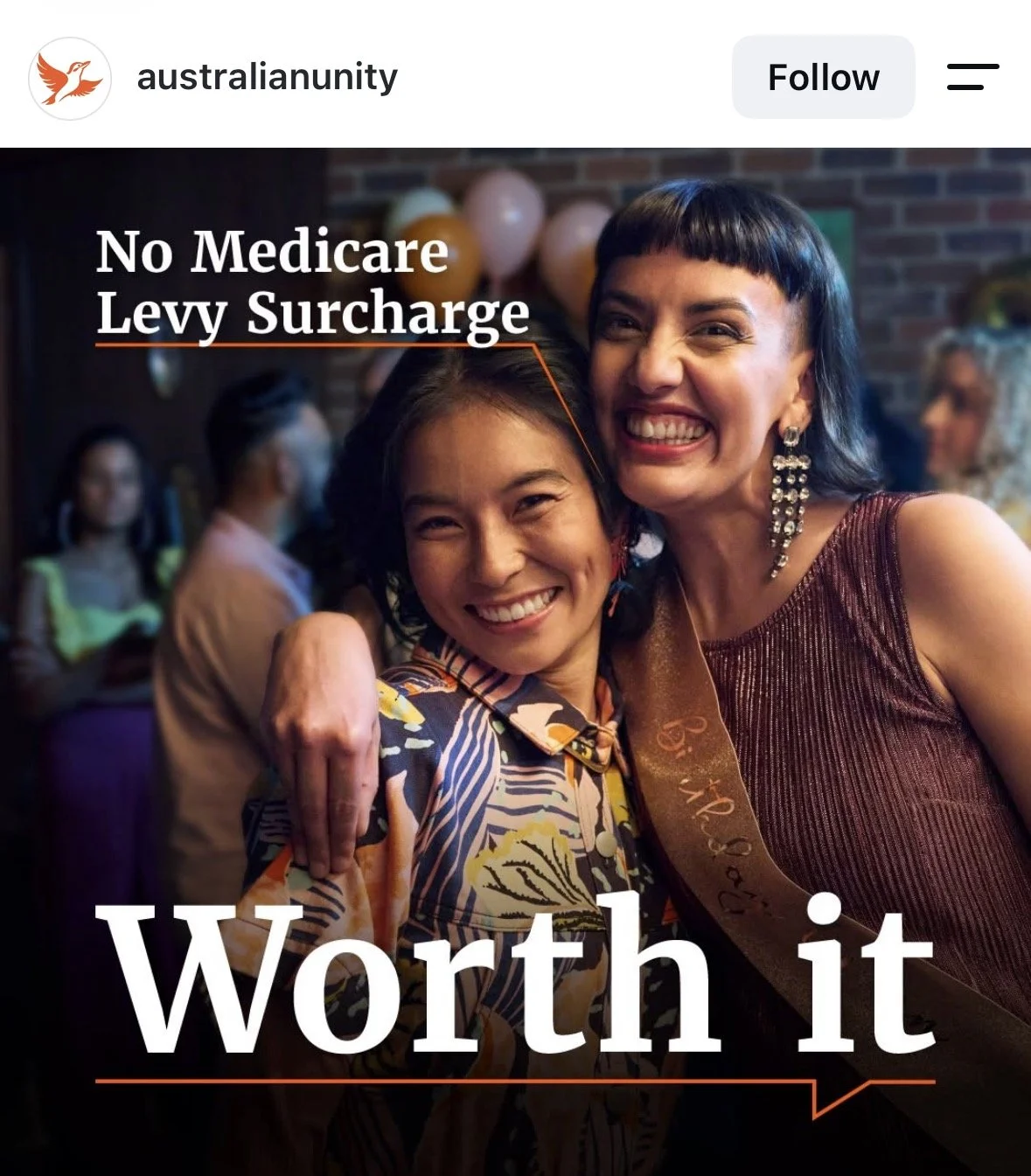 Two women smiling and hugging at a celebration event, with balloons in the background and a news banner that reads 'No Medicare Levy Surcharge' and 'Worth it'.