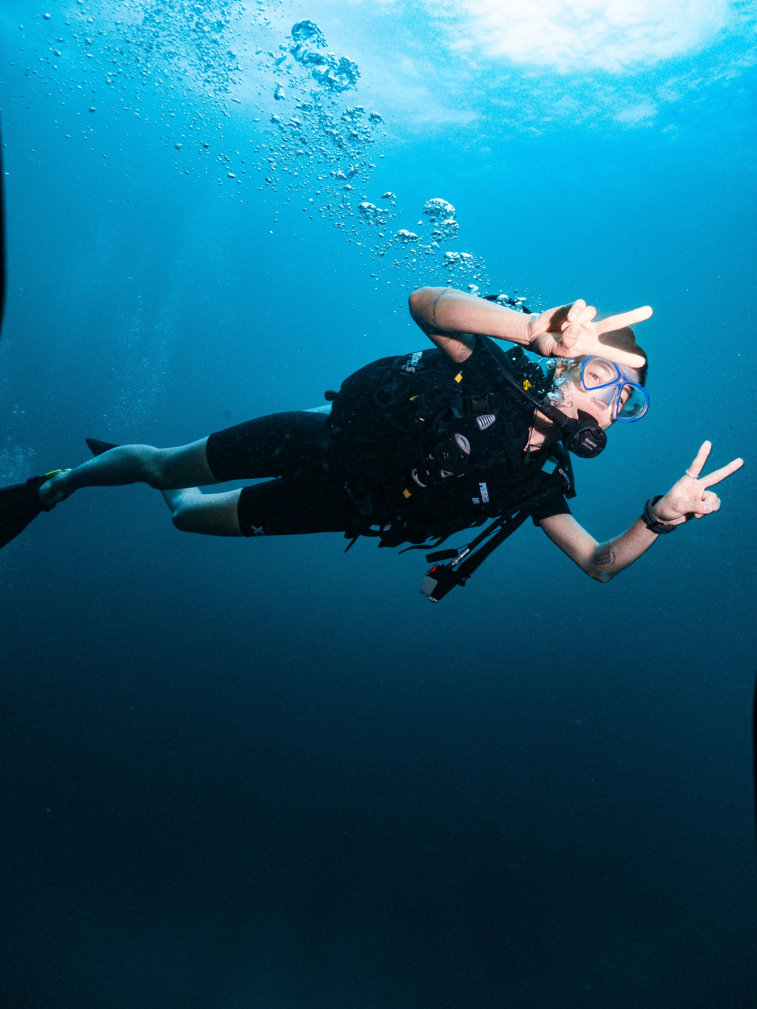 A woman scuba diving underwater, making Peace signs with both hands.