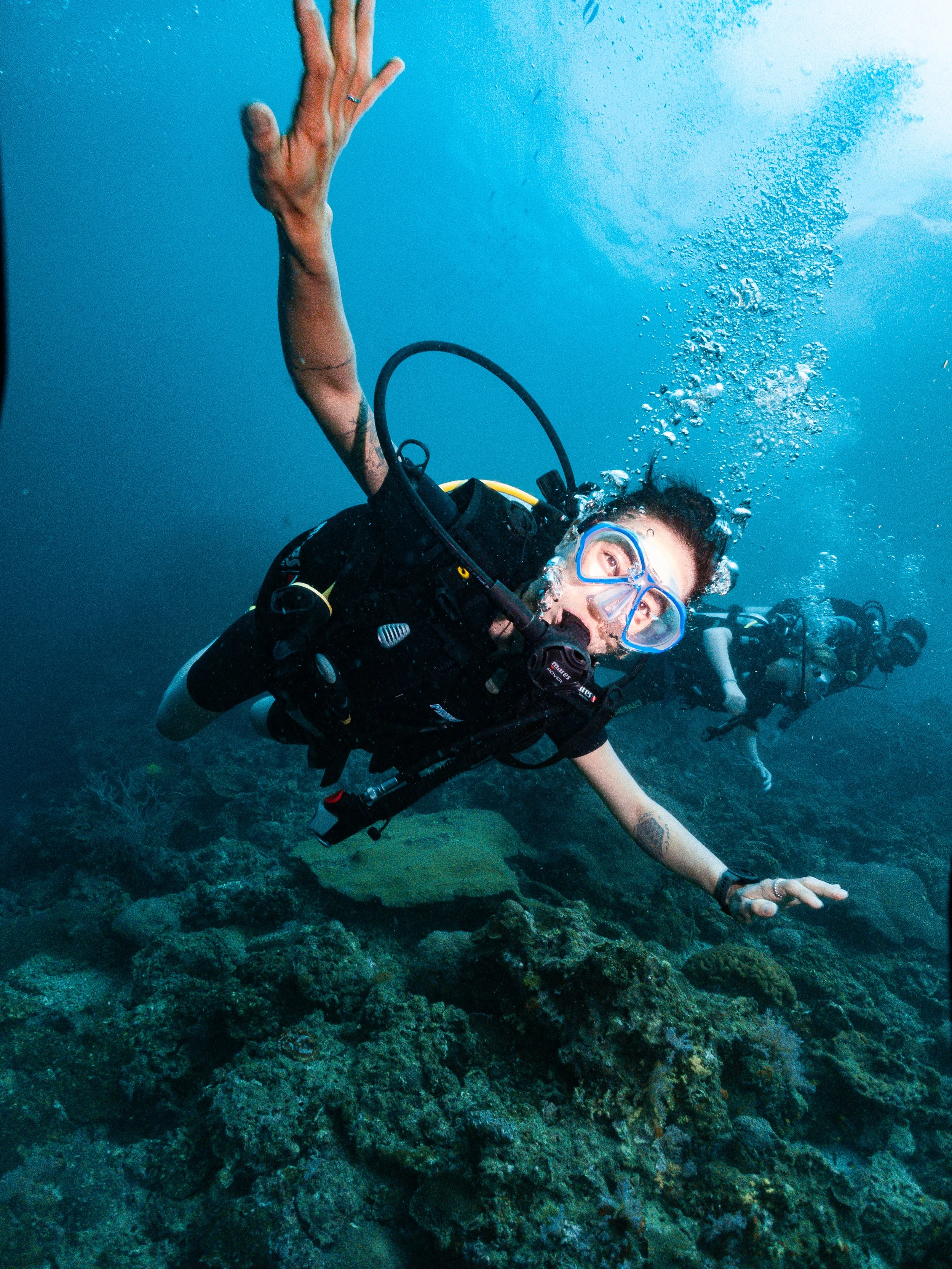 Person scuba diving underwater, reaching out towards the seabed, with a clear view of their face and diving equipment.