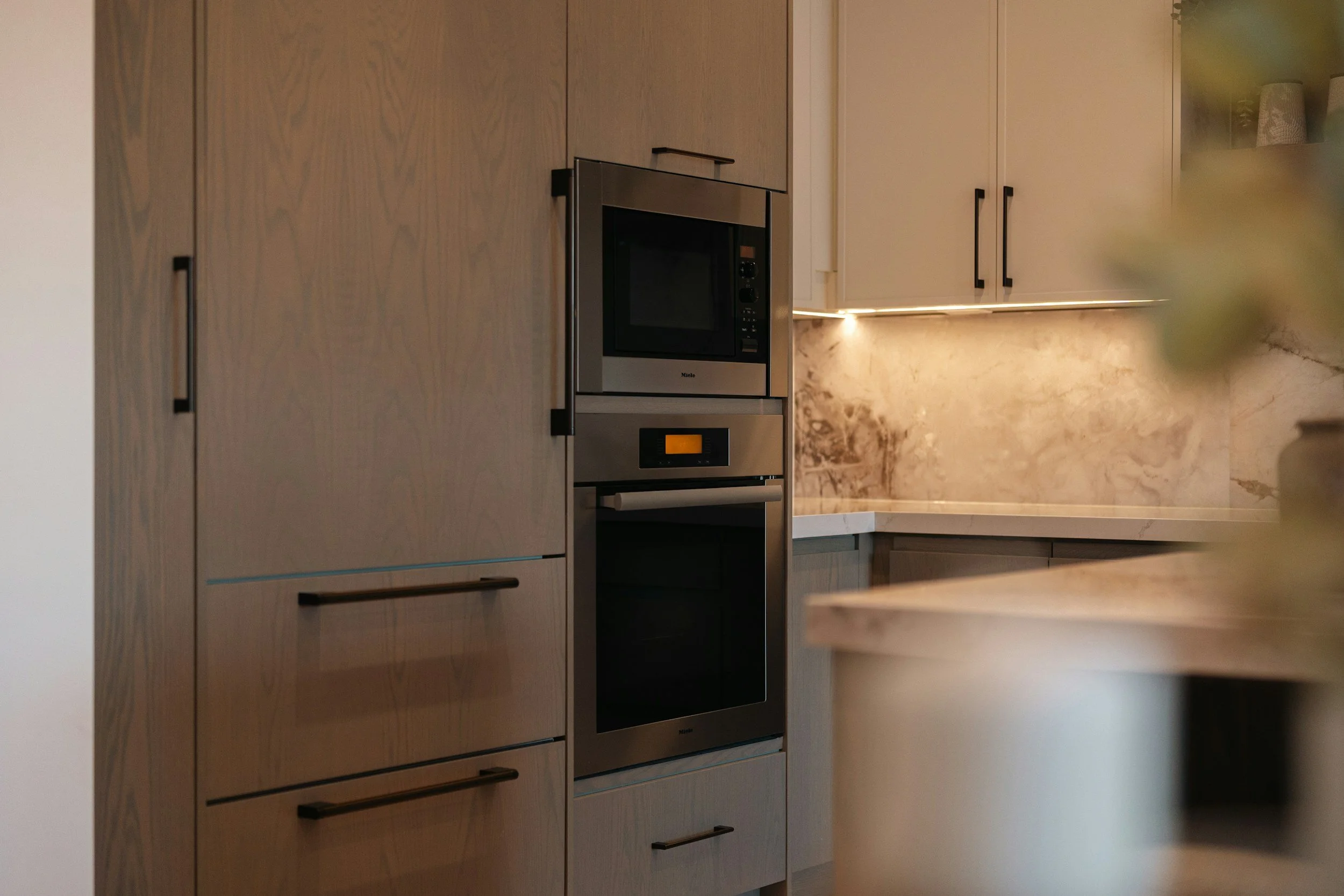 Modern kitchen with wood and white cabinets, built-in microwave oven, and a marble backsplash.