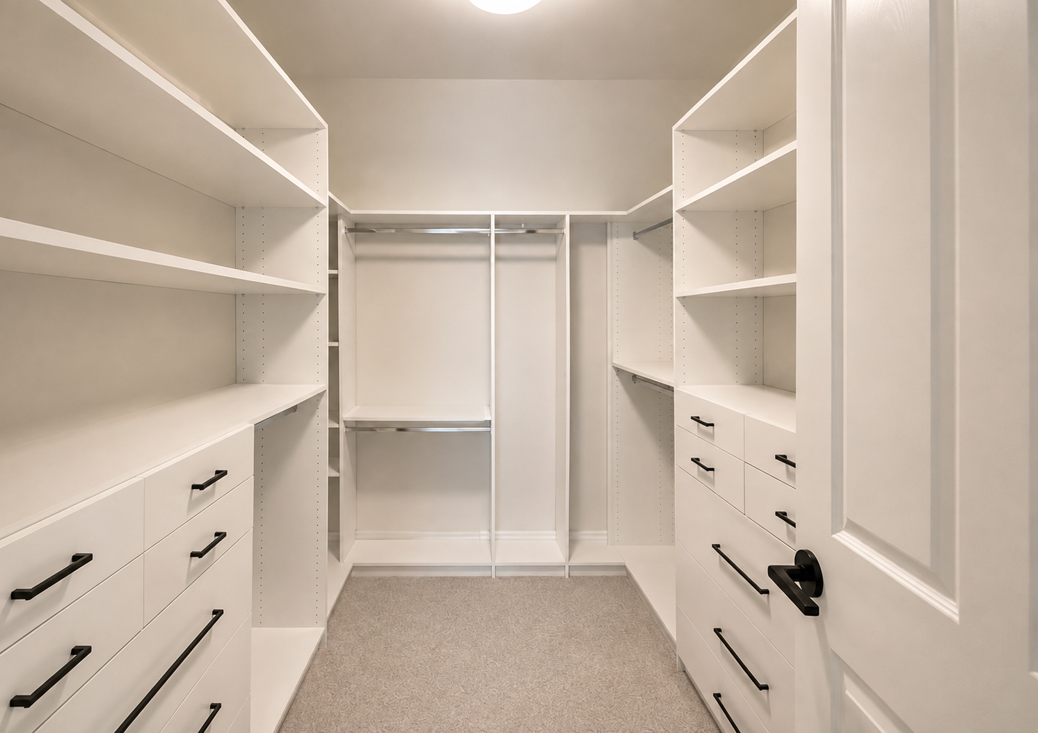 Custom white walk-in closet by Vanguard Cabinets featuring built-in shelving, hanging rods, drawers, and black hardware.