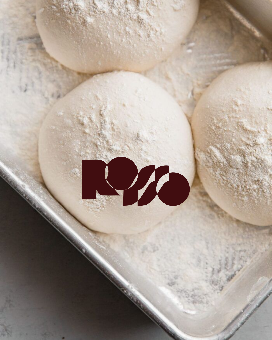 Dough balls dusted with flour in a metal tray with a logo overlay.