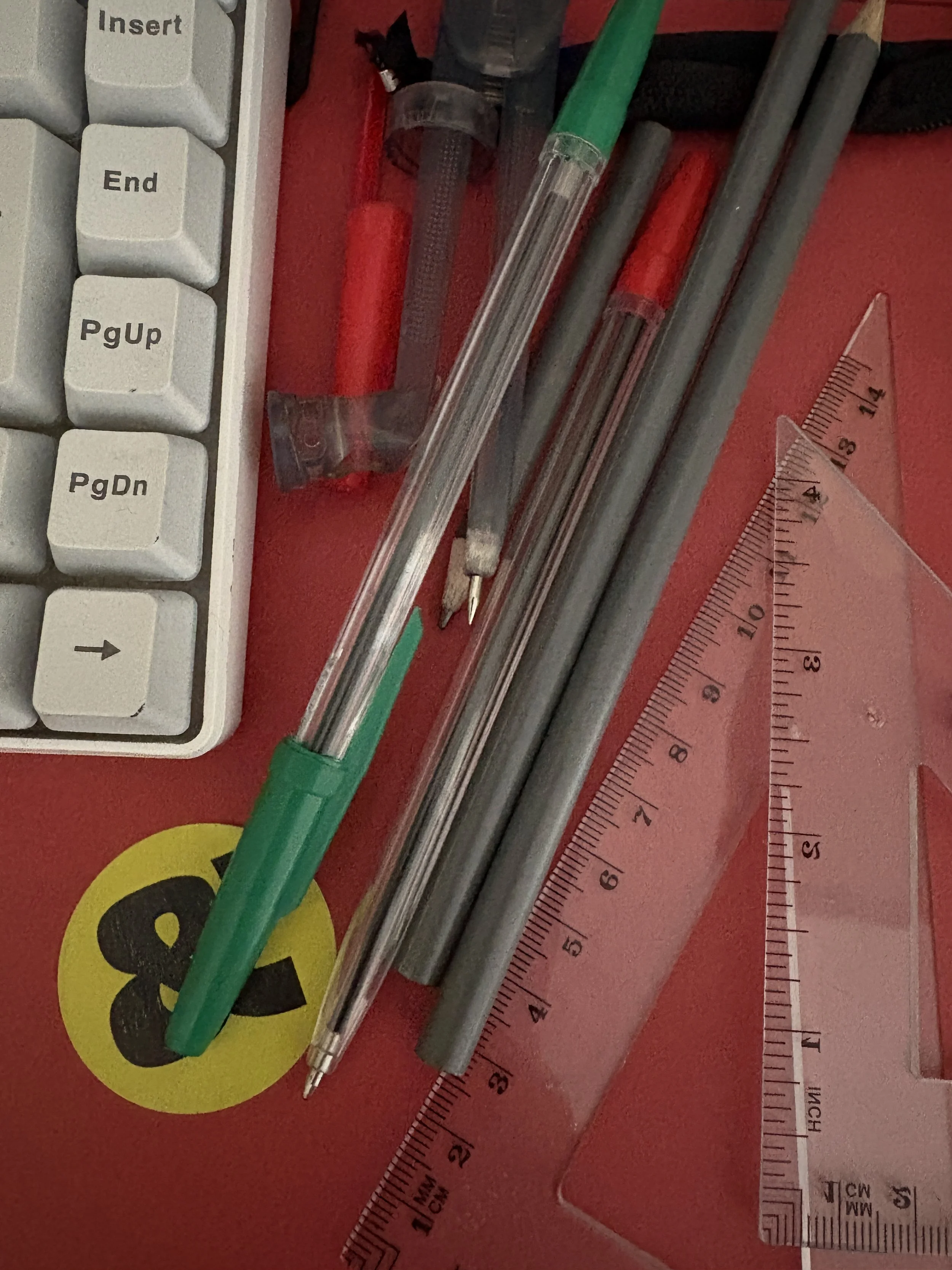 pens, pencils, rulers and a keyboard on a red backgrouns with a green and black circle sticker