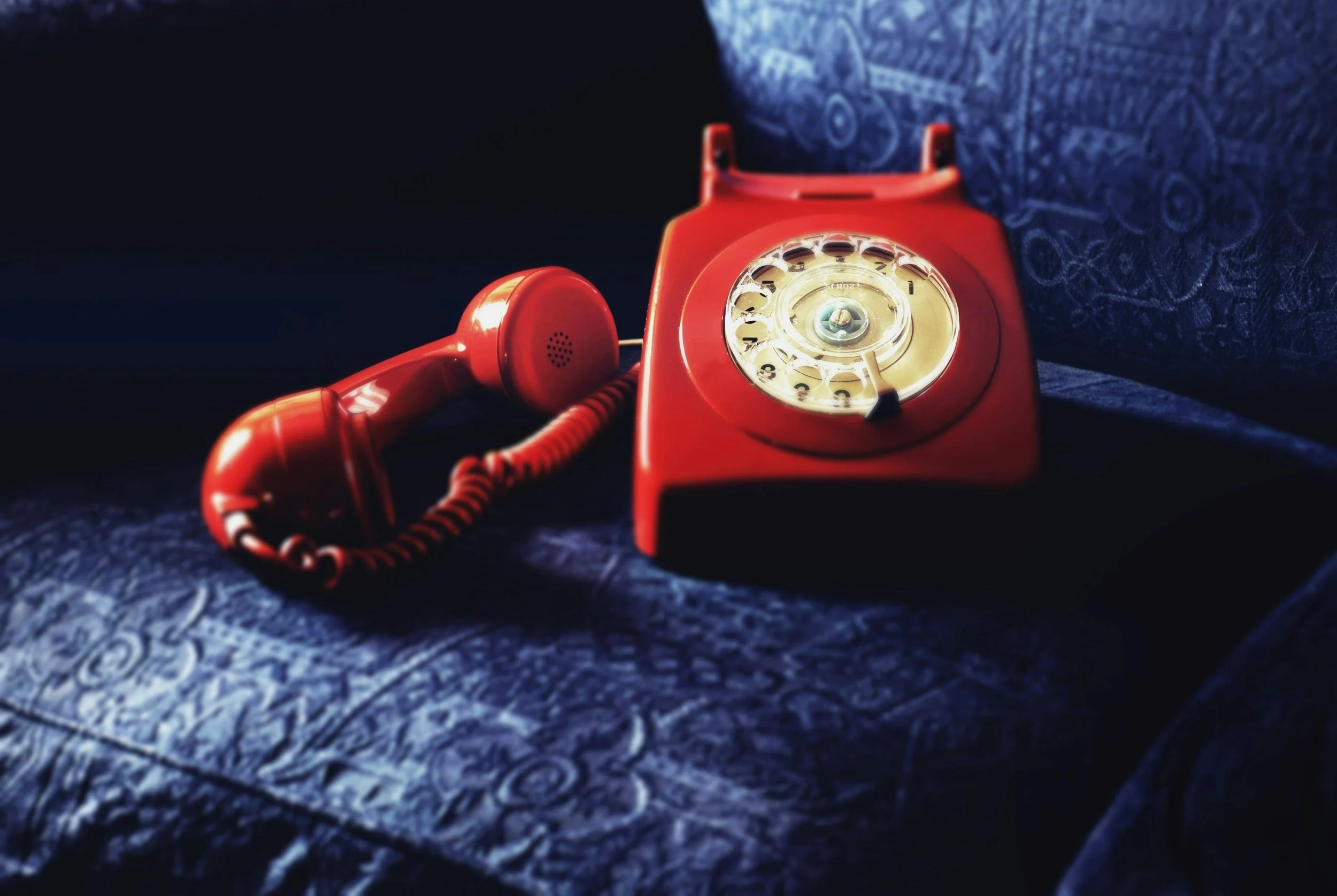 red landline, top handle telephone on a blue sofa cushion.