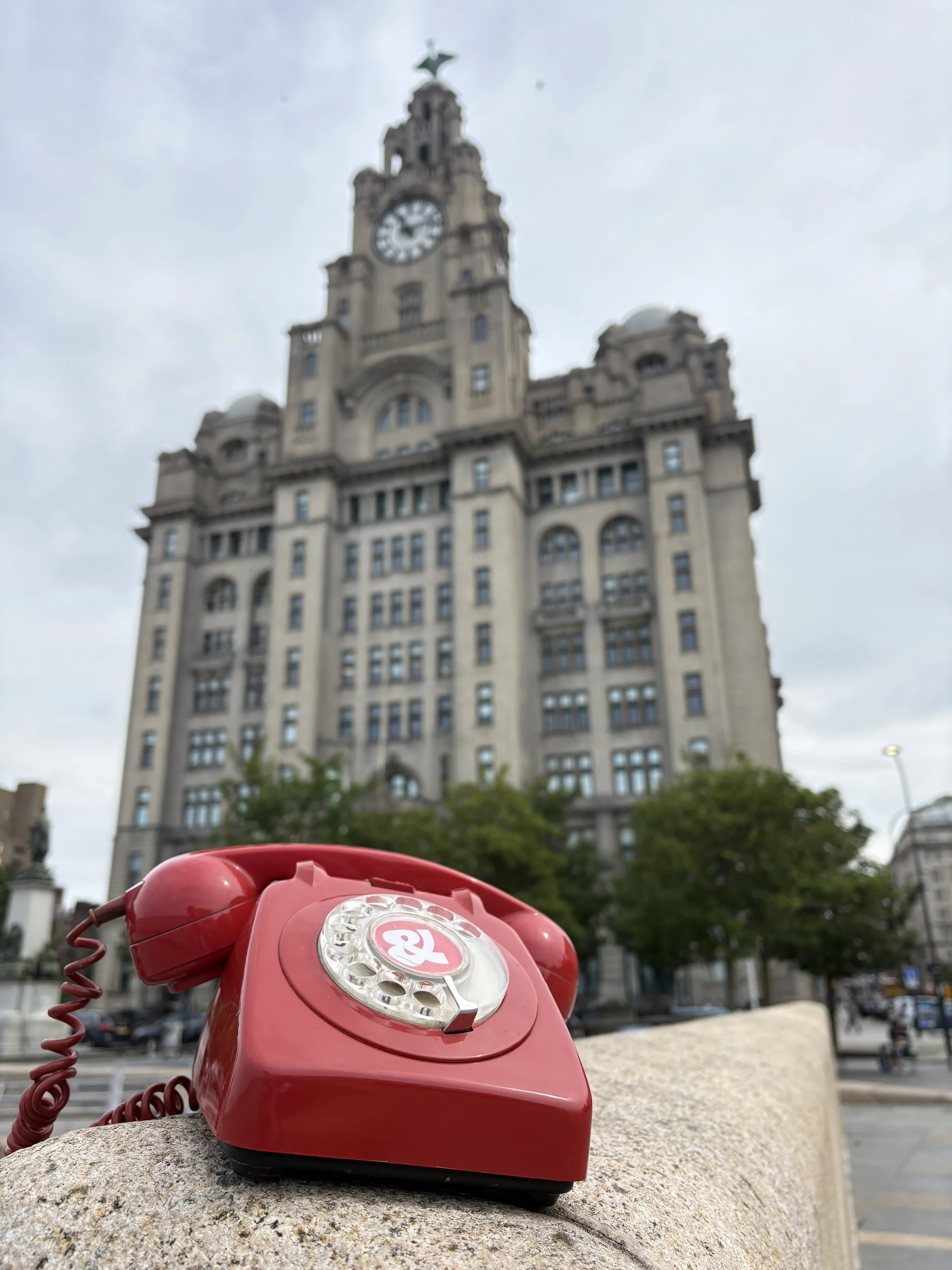 Royal Liver Building blurred in the background with a red rotary phone in the foreground