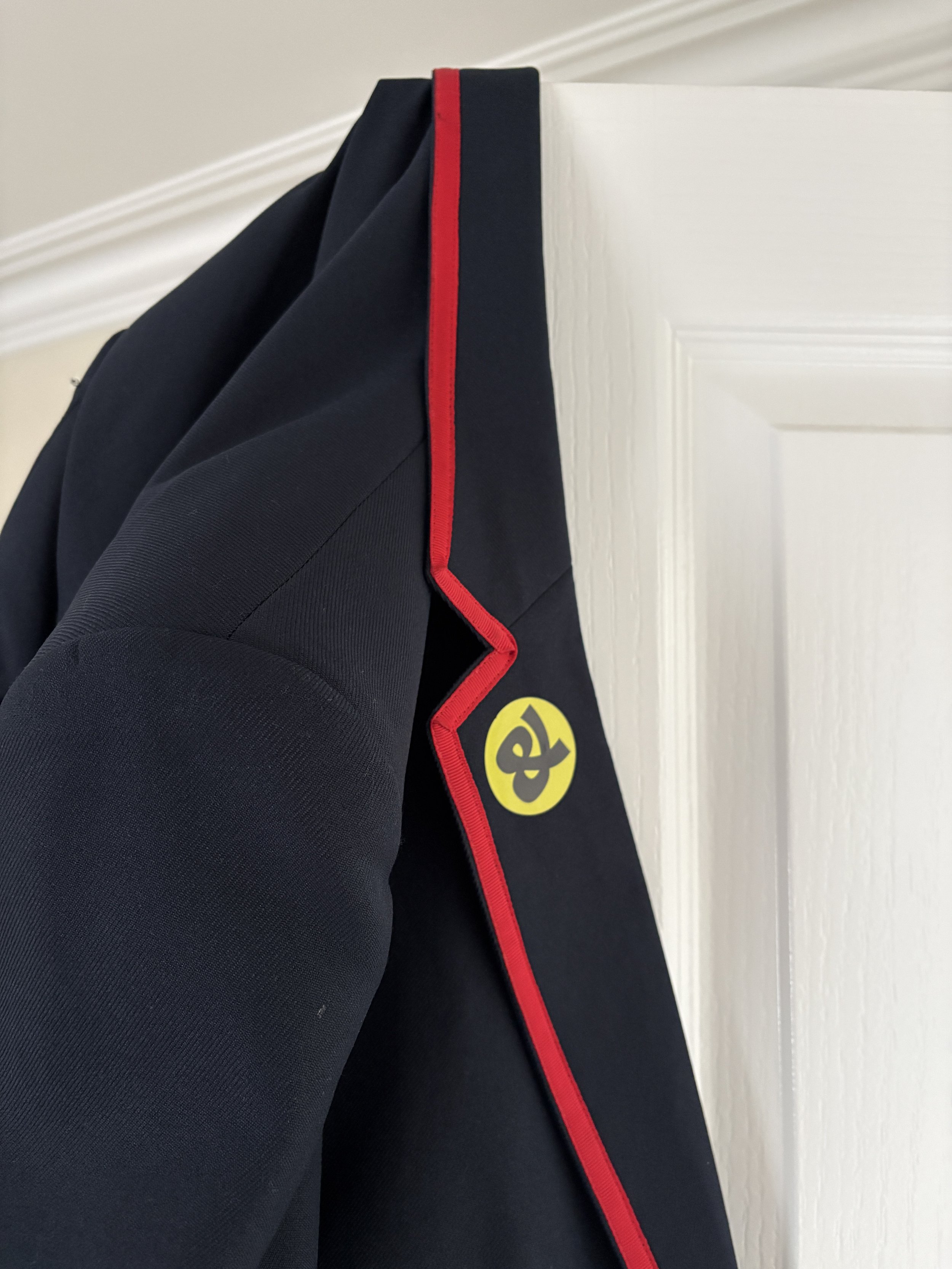 navy and red blazer shoulder hanging on white door. Green and black circle sticker on the lapel