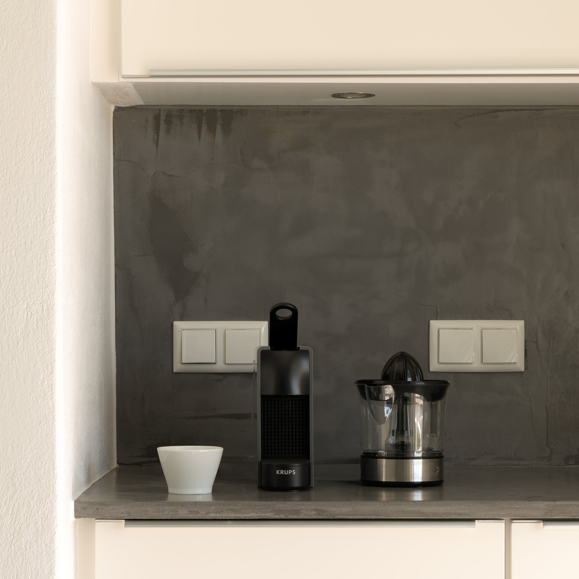 Contemporary kitchenette with premium coffee amenities and stone backsplash.