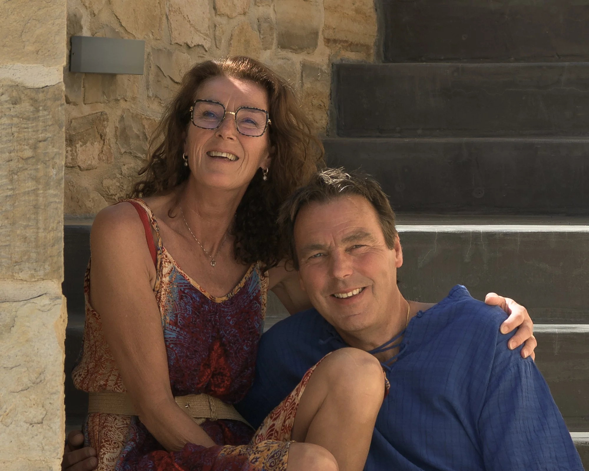 Hosts of Galini Breeze sitting together outside a traditional stone house in South Crete, reflecting the warm and personal atmosphere of the adults-only resort near Agia Galini