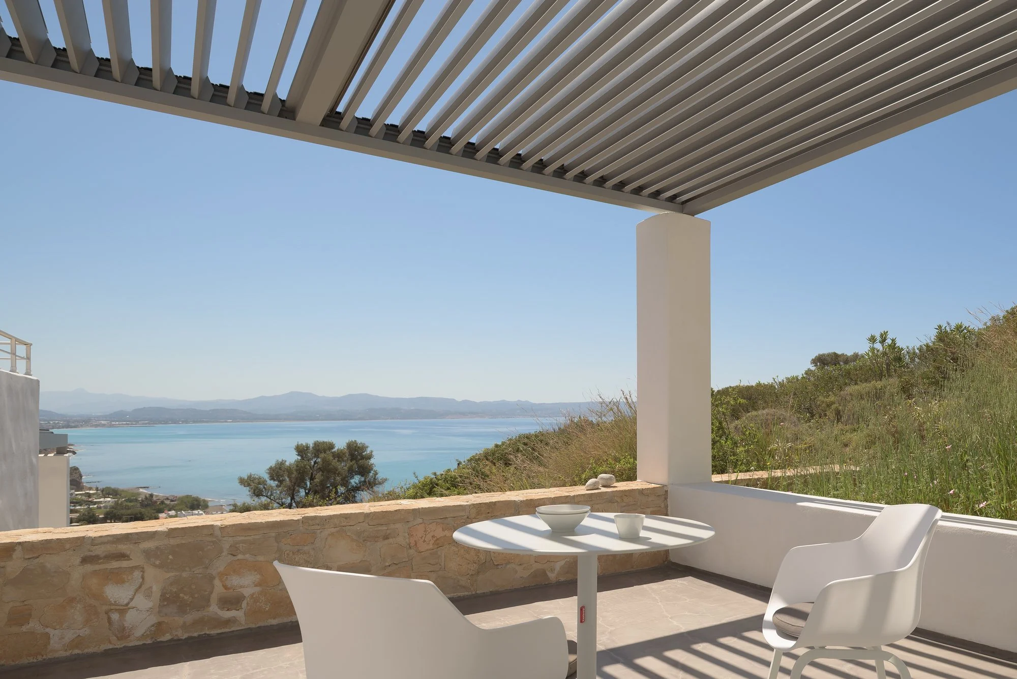 Minimalist pergola lounge with panoramic hillside and sea views.