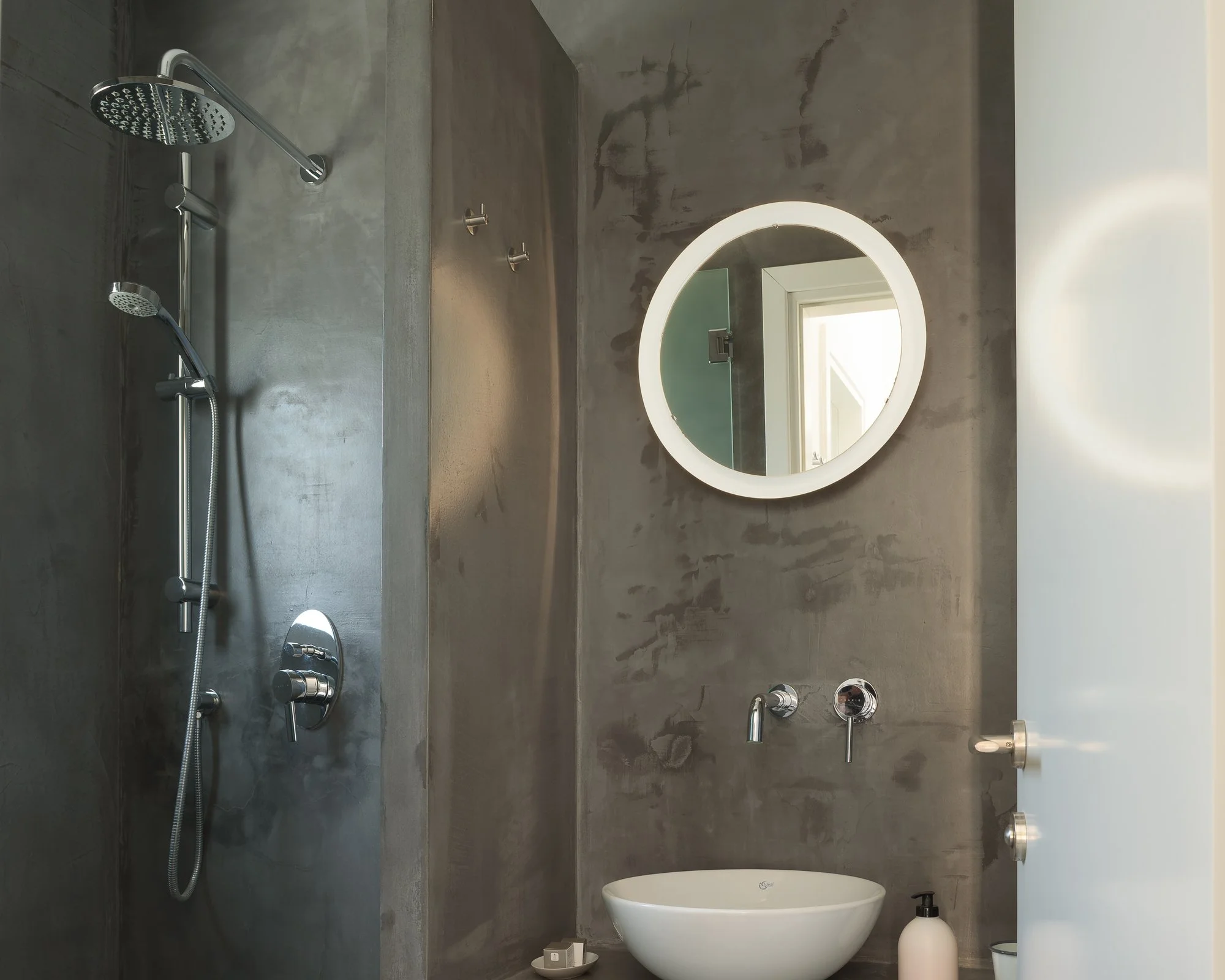 Modern concrete bathroom with circular mirror and luxury boutique finishes.