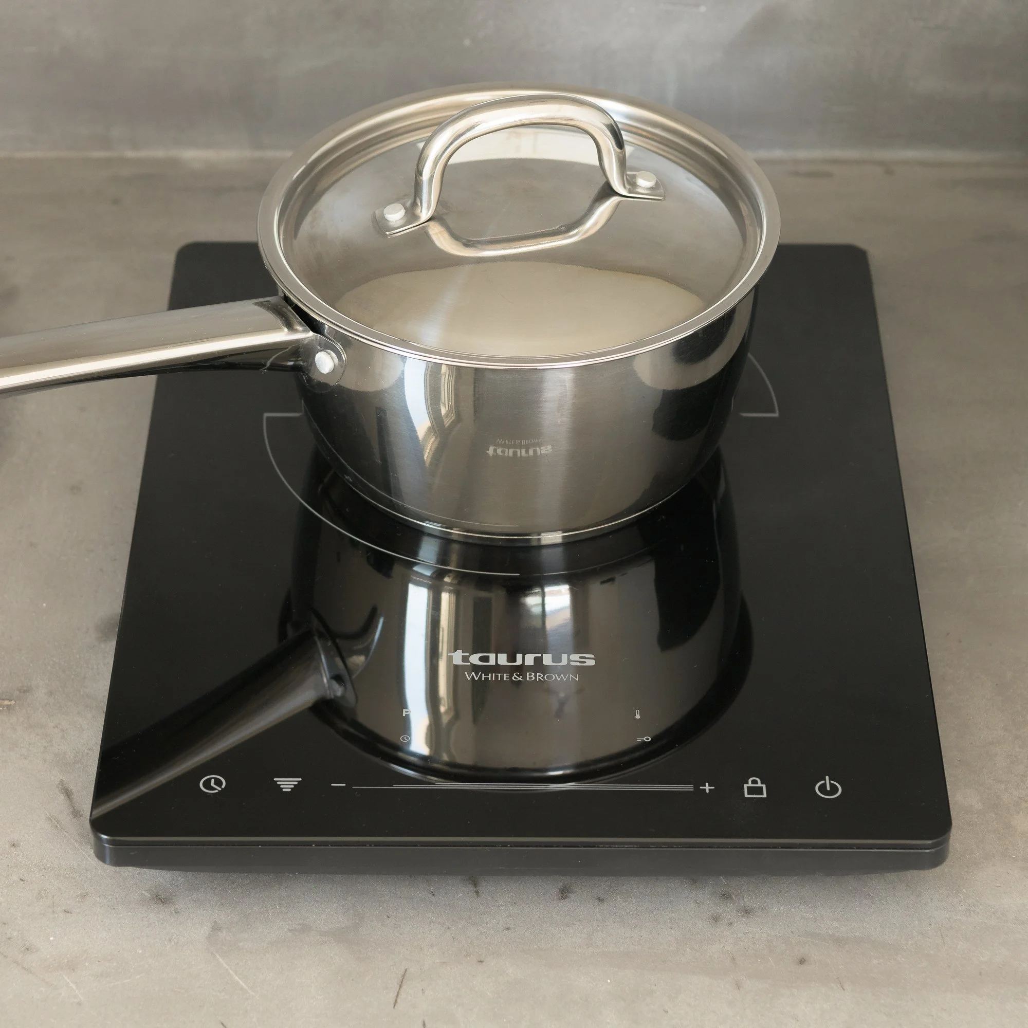 Stainless steel saucepan with a handle and glass lid on an induction cooktop.
