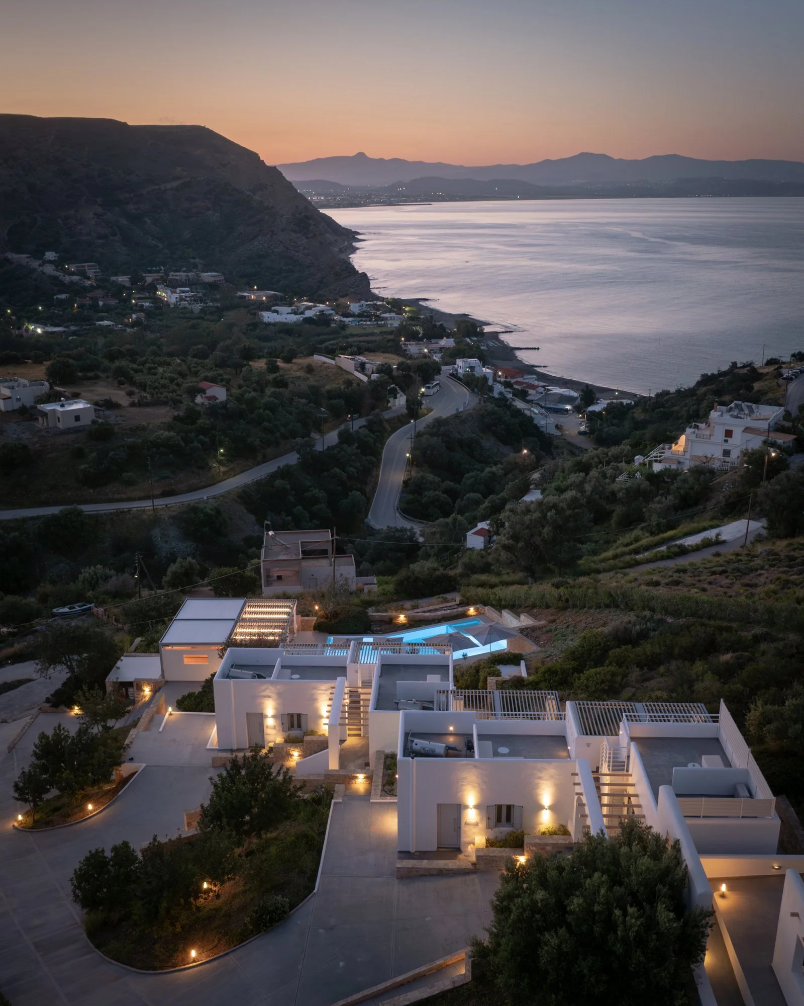 Evening aerial view of Galini Breeze studios, overlooking Agia Galini and the Libyan Sea at sunset with hills in the background.