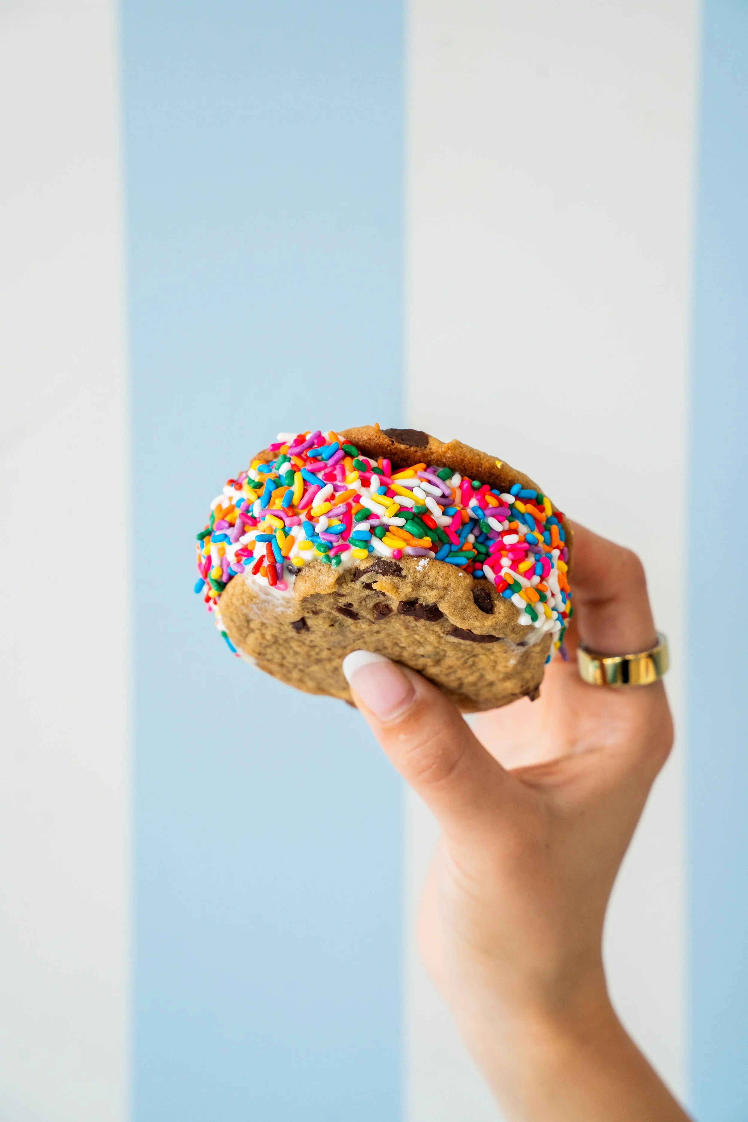 Hand holding a cookie with colorful sprinkles against a blue and white striped background.