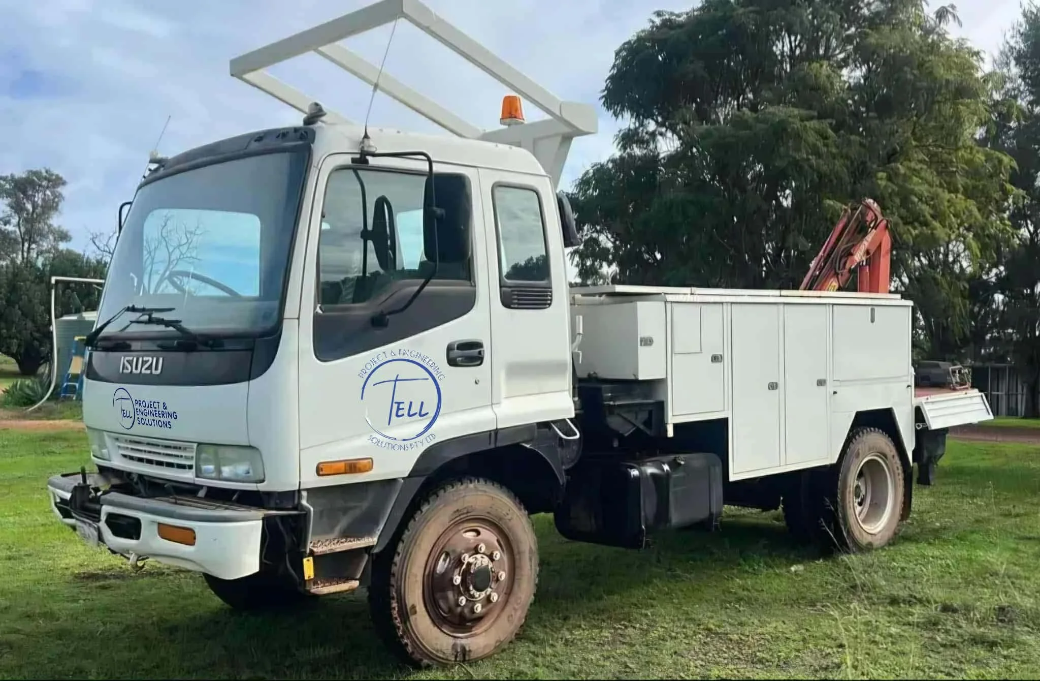 White utility truck with a logo that says 'PROJECT & ENGINEERING SOLUTIONS' on the side, parked on grass near trees, with a hydraulic crane arm folded on the back, and an orange warning light on the roof.