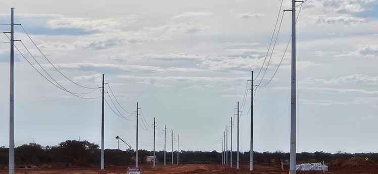 Image of a rural area with power poles and power lines extending into the distance under a cloudy sky.