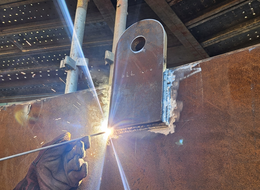 A worker welding a metal joint inside a construction site, with sparks flying from the welding process.